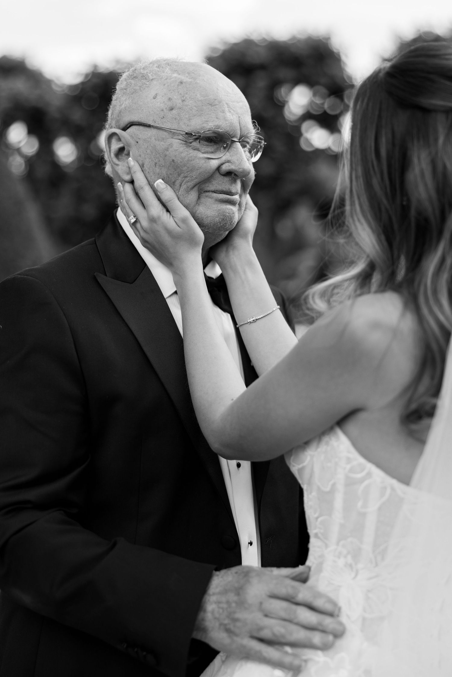 Black and white photo of a bride tenderly cupping an elderly mans face at a wedding ceremony.