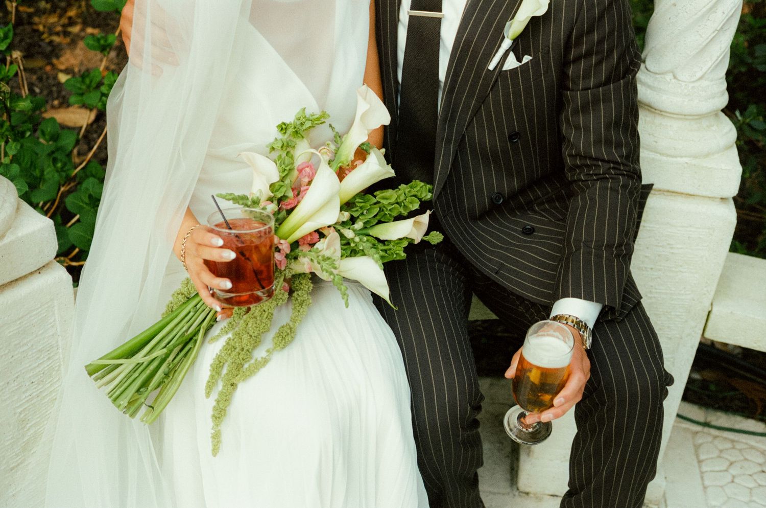 A close up image of a bride and groom's hands holding cocktails