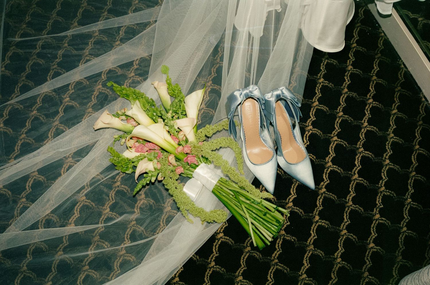 A film photo of a wedding bouquet and blue heels on top of a veil