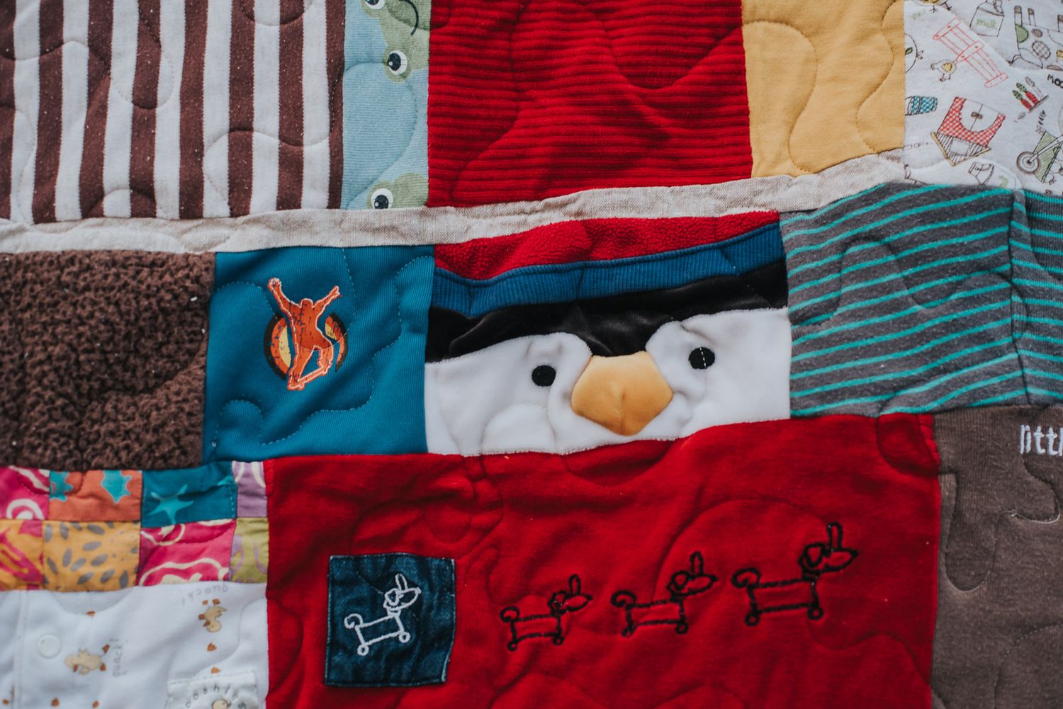 Colourful memory quilt made with clothes, focused on a section with a penguin that was a hat converted into a square in 
