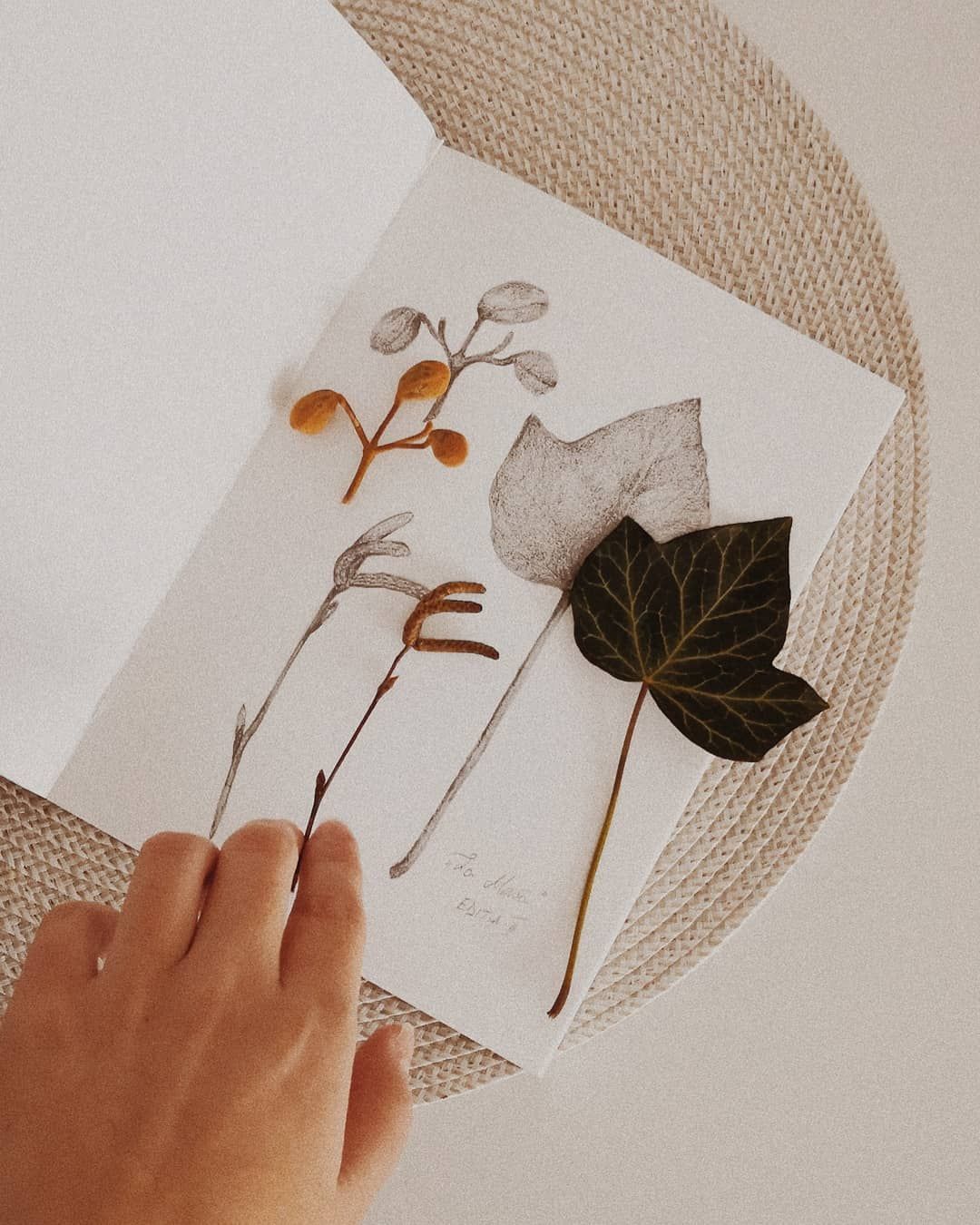 Hand turning pages of botanical illustrations in an art book on beige background.