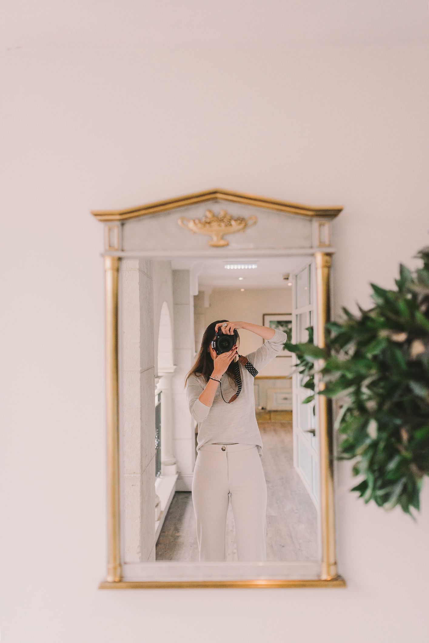 Person taking selfies in an ornate gold-framed mirror against white walls.
