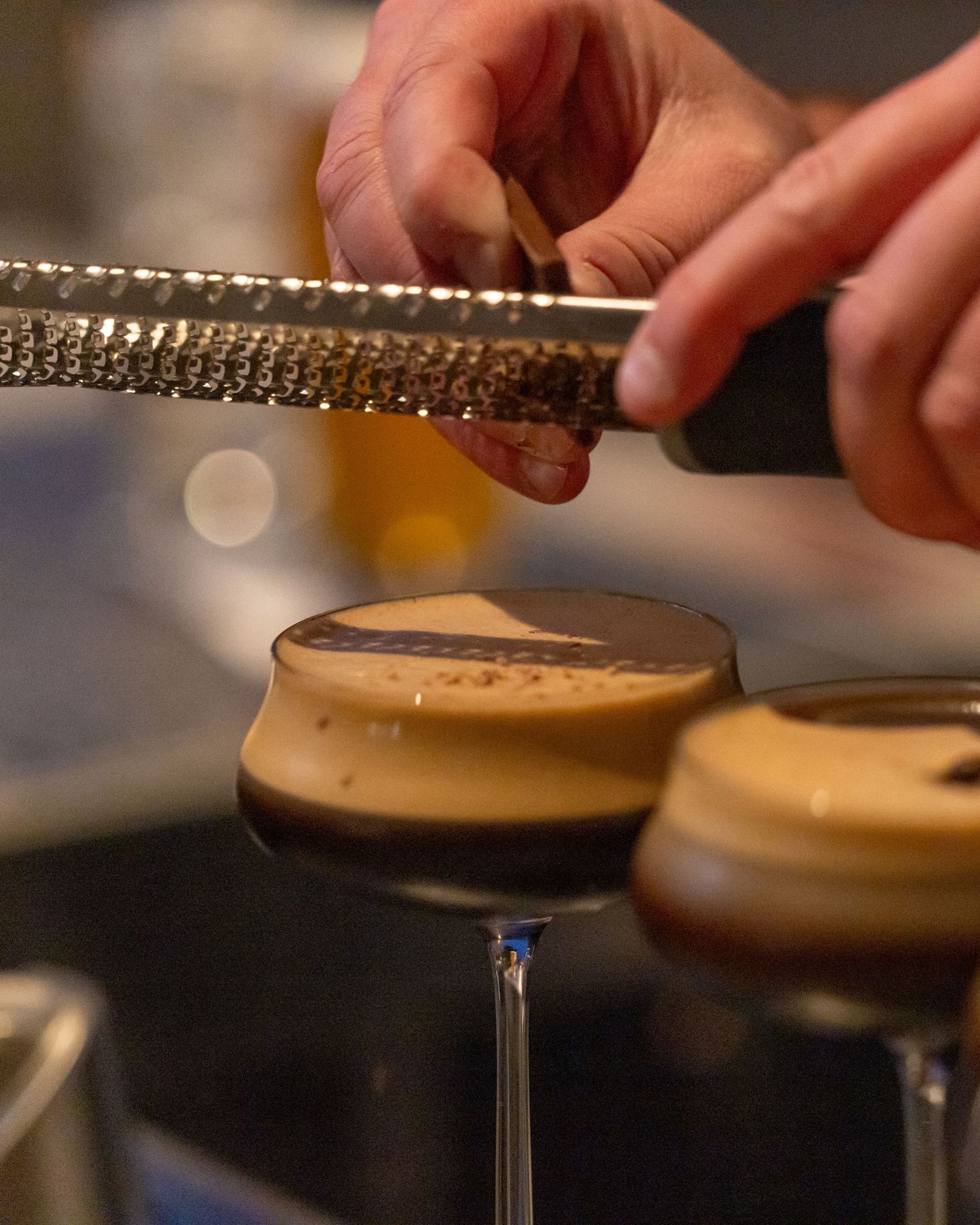Bartender grating garnish over espresso martini cocktails.