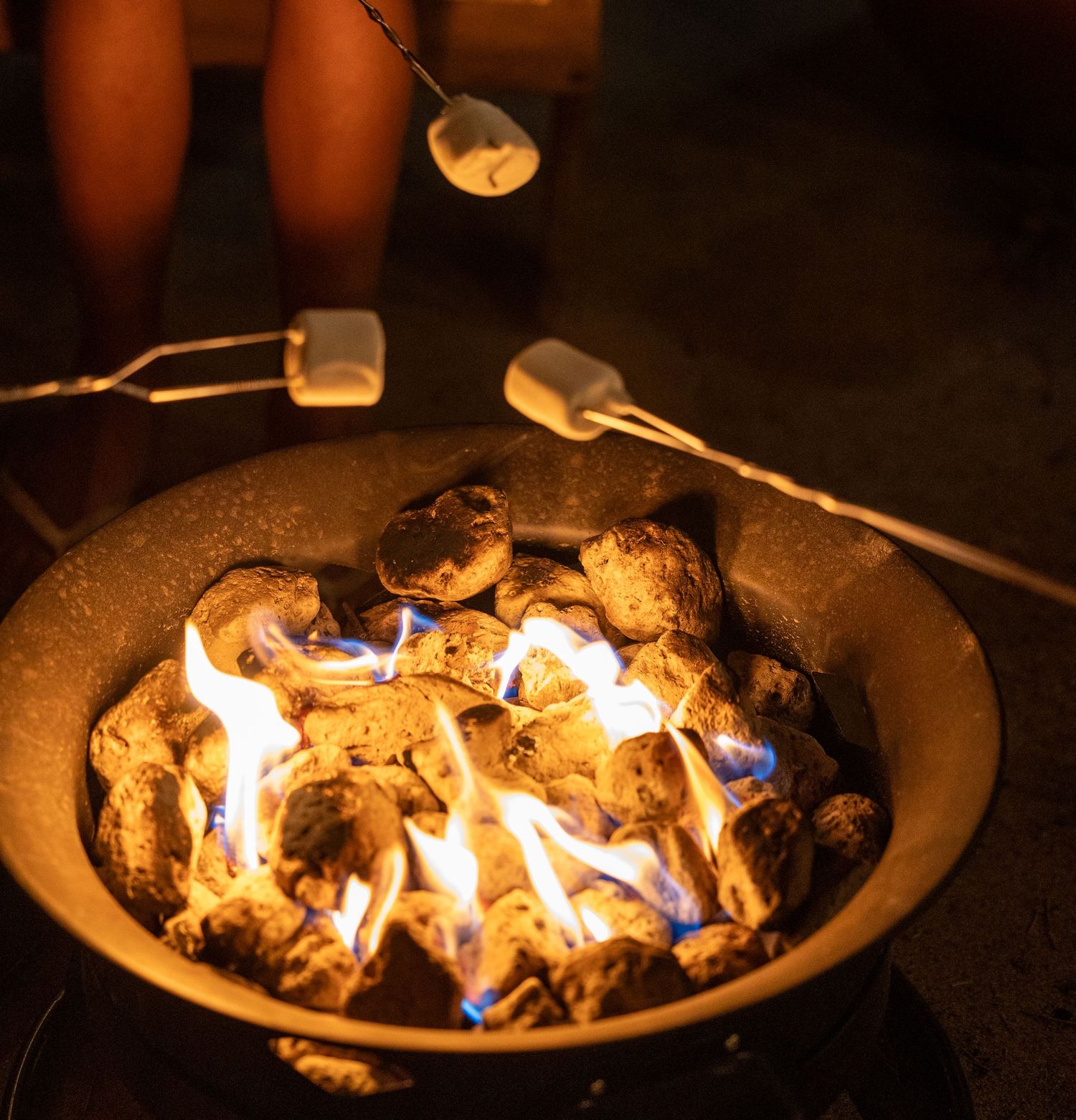 People roasting marshmallows on skewers over a glowing outdoor fire pit at night.