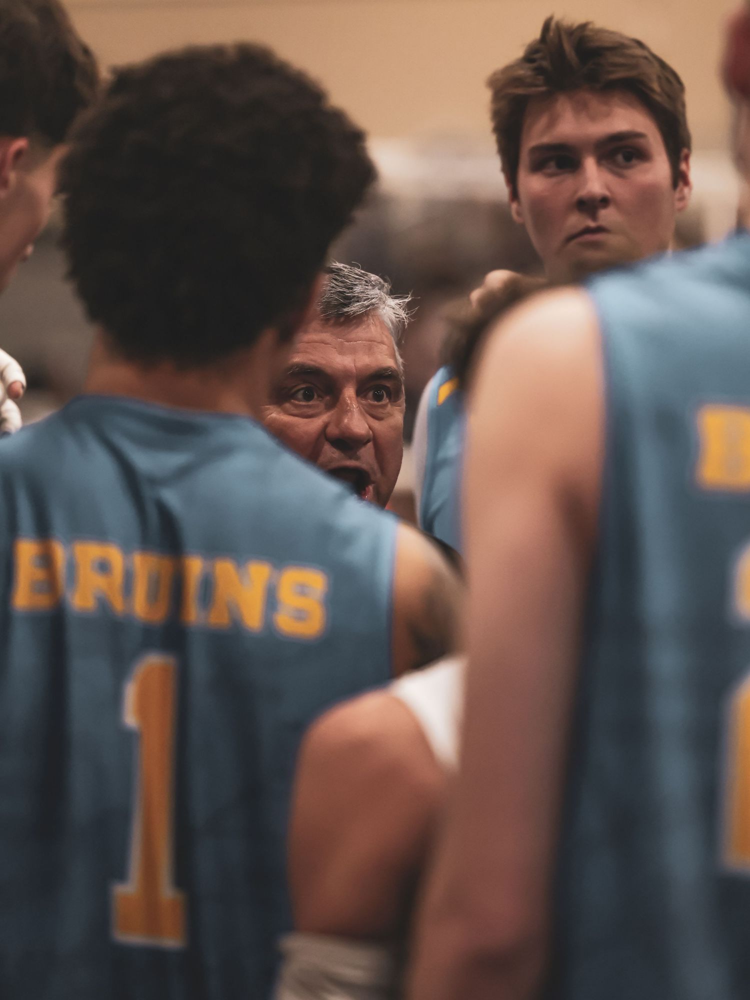 Basketball coach huddles with Bruins team players wearing blue jerseys during a timeout or halftime talk.
