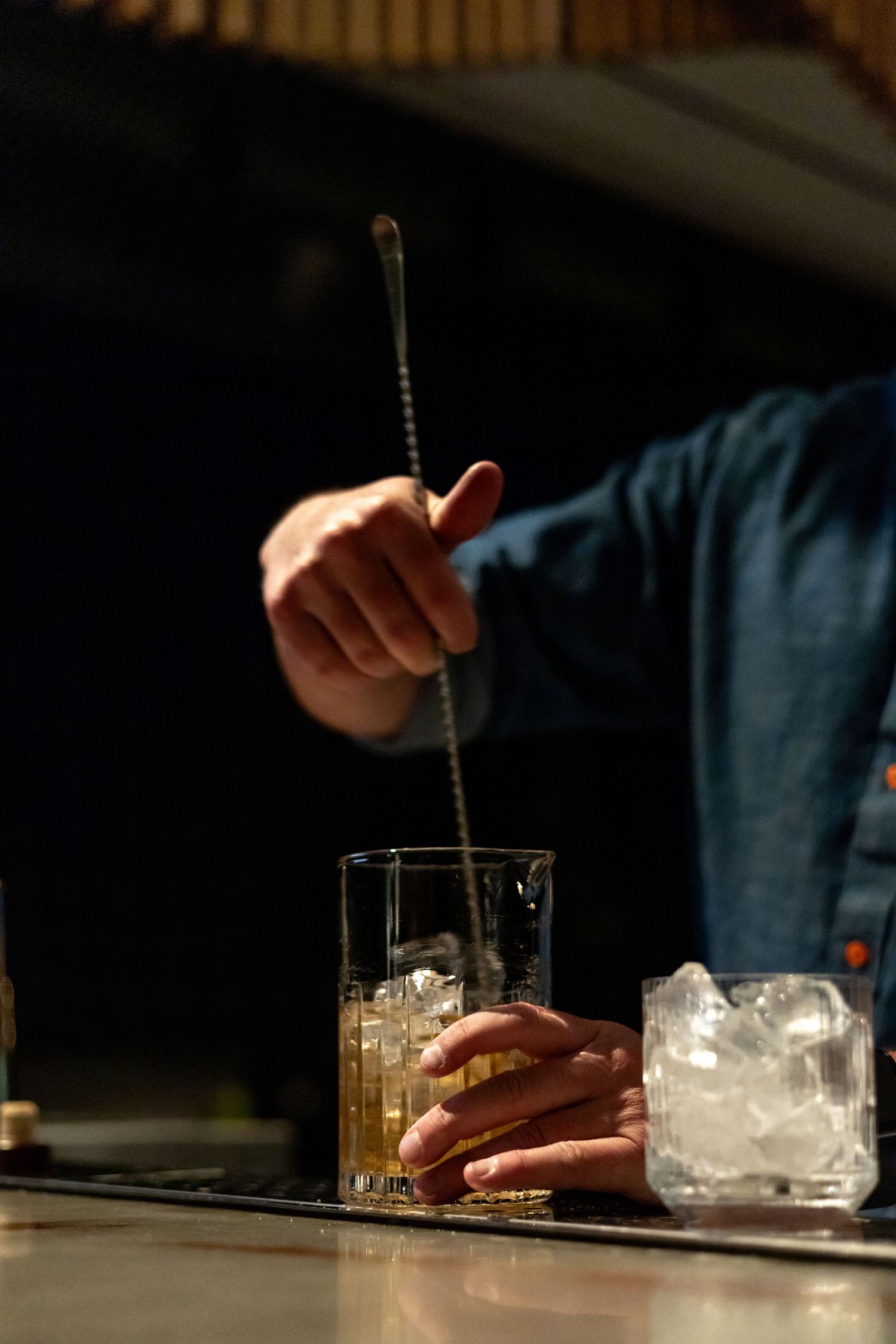 Bartender stirring whiskey cocktail with ice in glass.