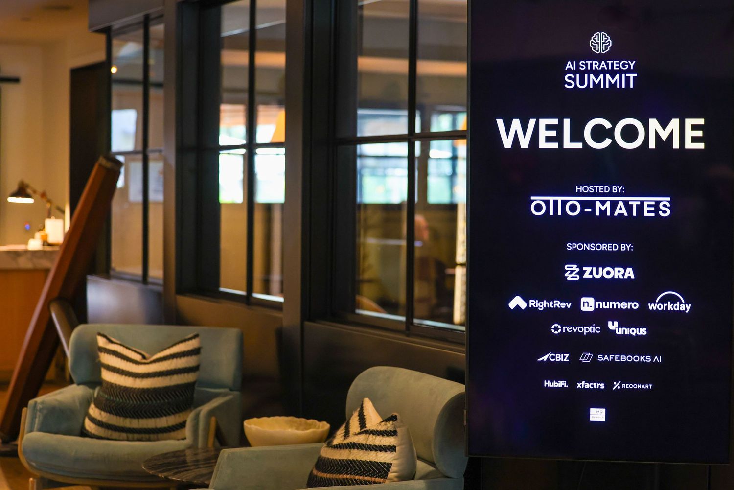 AI Strategy Summit welcome sign hosted by Otto-Mates, sponsored by Zuora and other tech companies, displayed in a modern lounge.