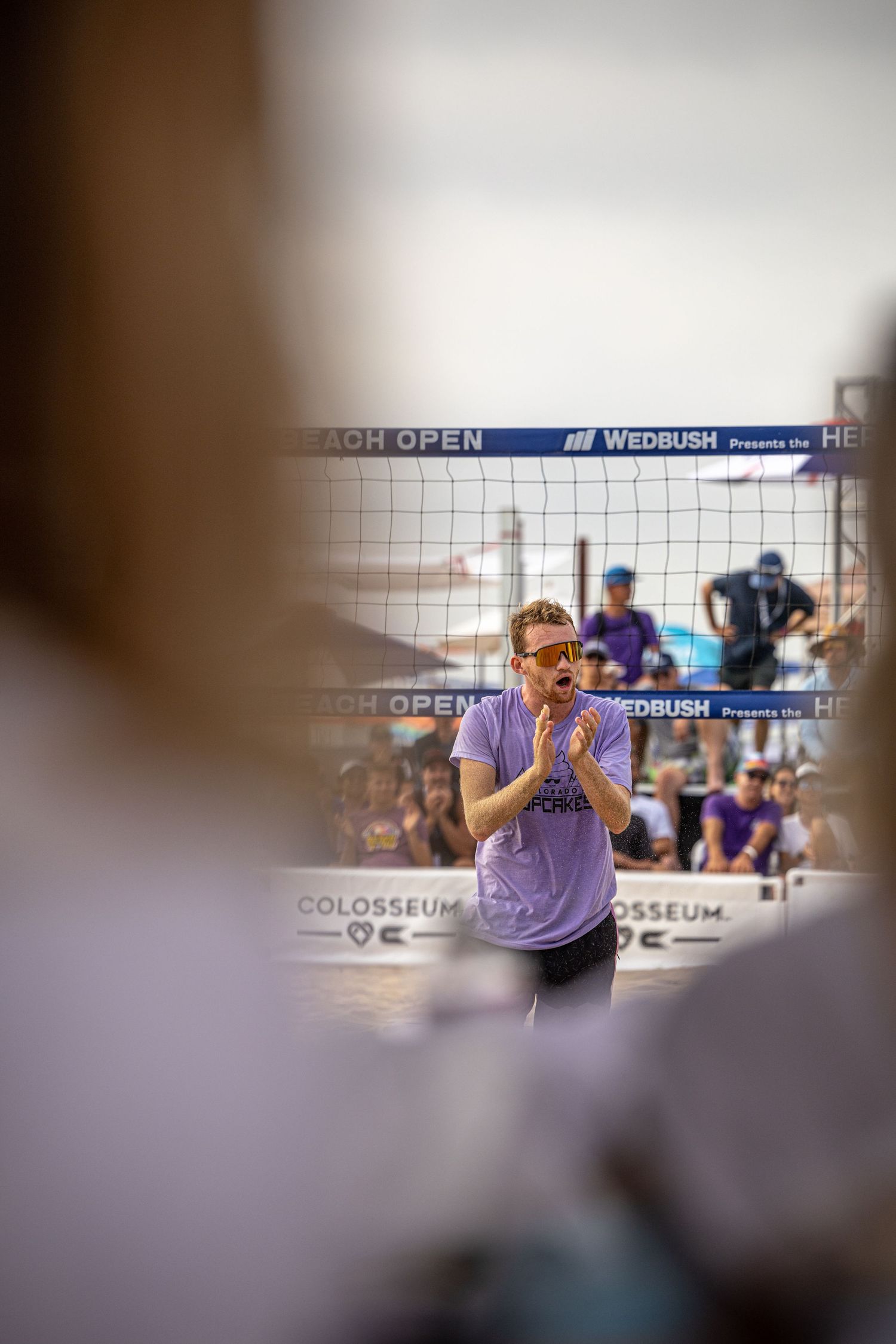A player in a purple shirt claps hands at a Wedbush Beach Open volleyball tournament.