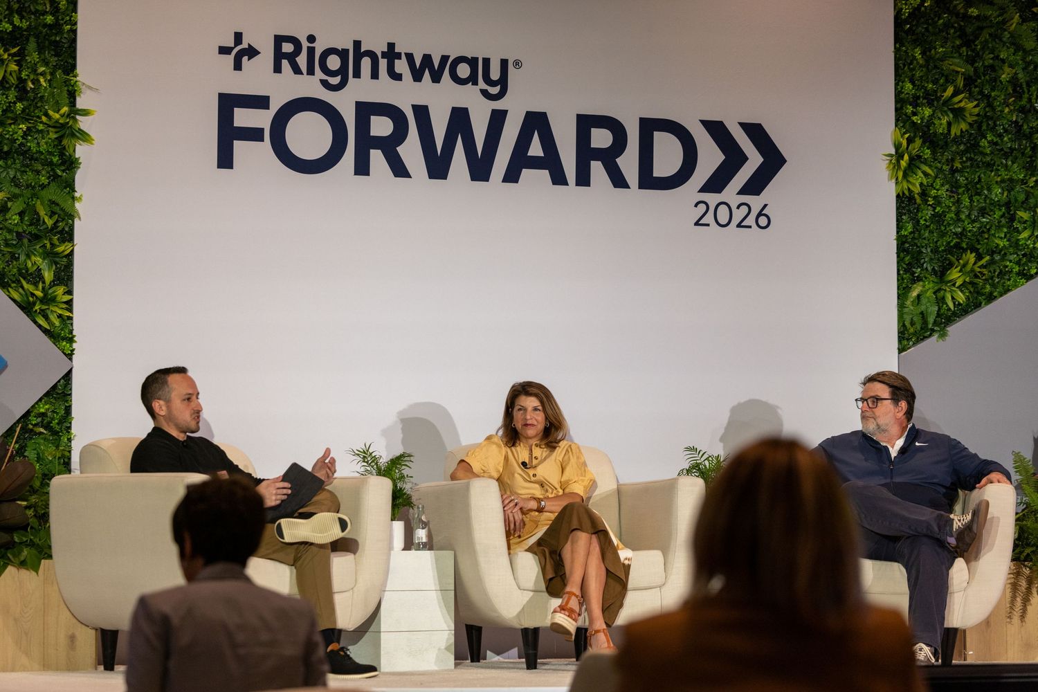 Three panelists discuss at Rightway Forward 2026 conference, seated in white chairs on a modern stage with green backdrop.