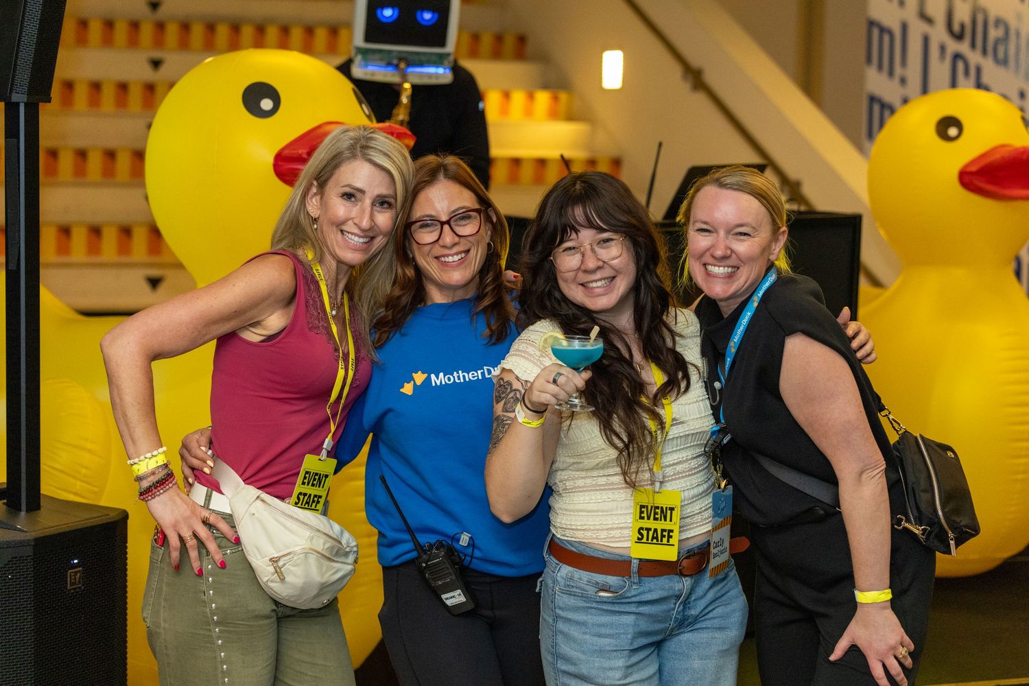 Four women smiling at an event with large yellow rubber ducks, one wearing a MuleSoft blue shirt.