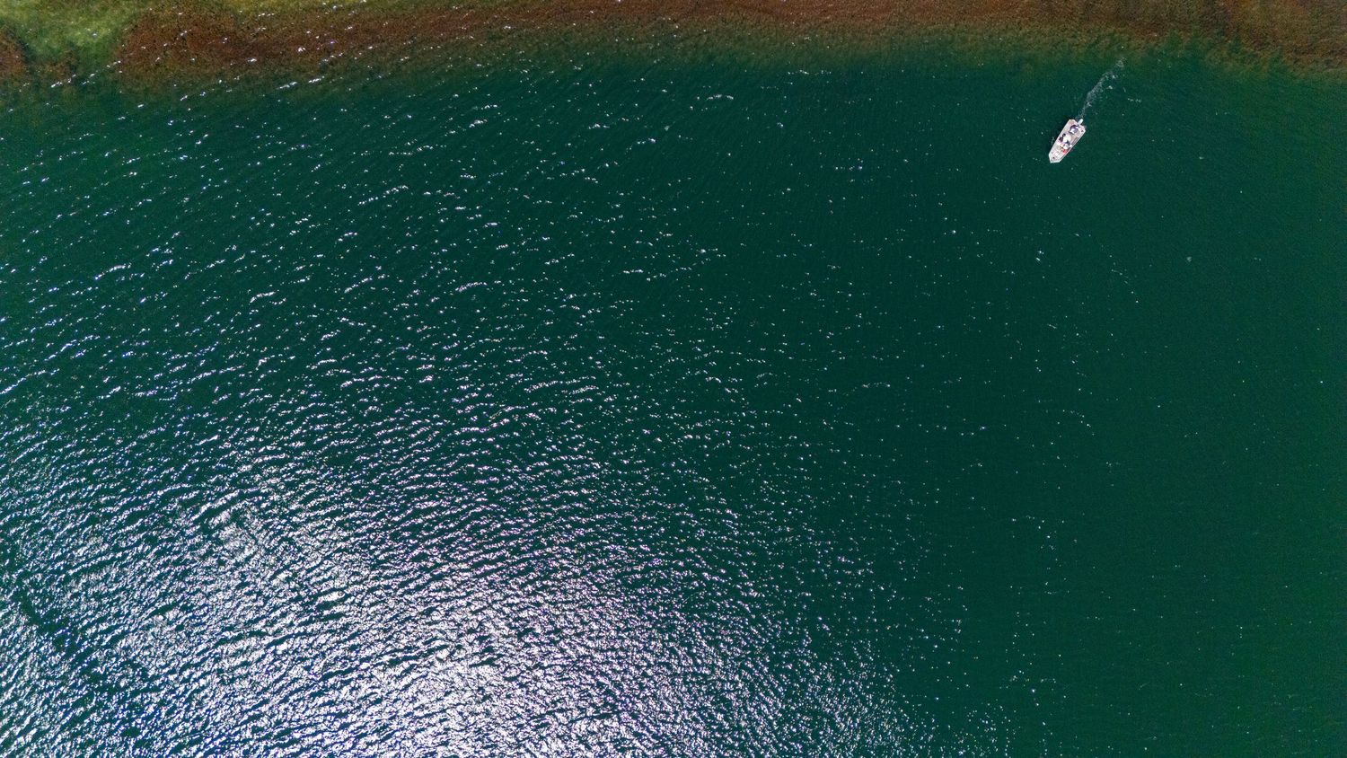 Aerial drone view of a white sailboat gliding across deep teal-green lake water.