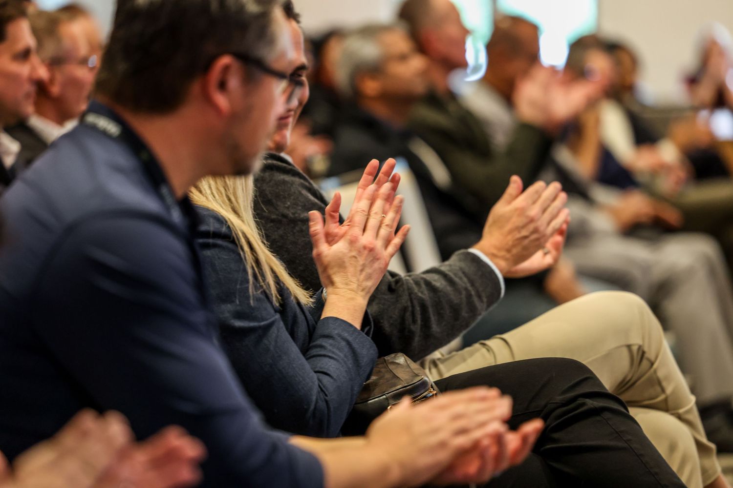 Audience members clapping and applauding at a professional conference or business event indoors.