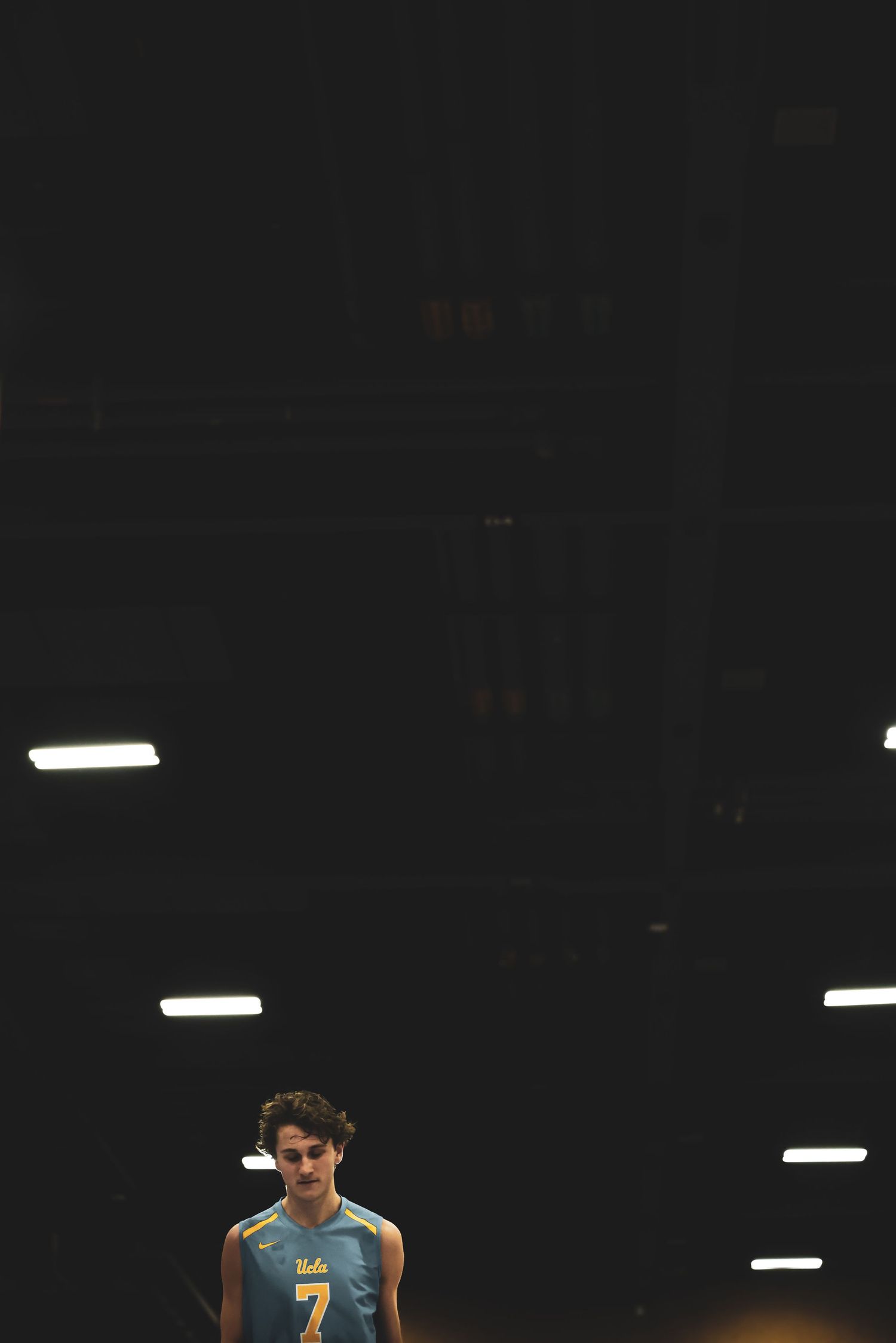 UCLA Bruins player wearing jersey number 7 stands on a dimly lit volleyball court during a match.