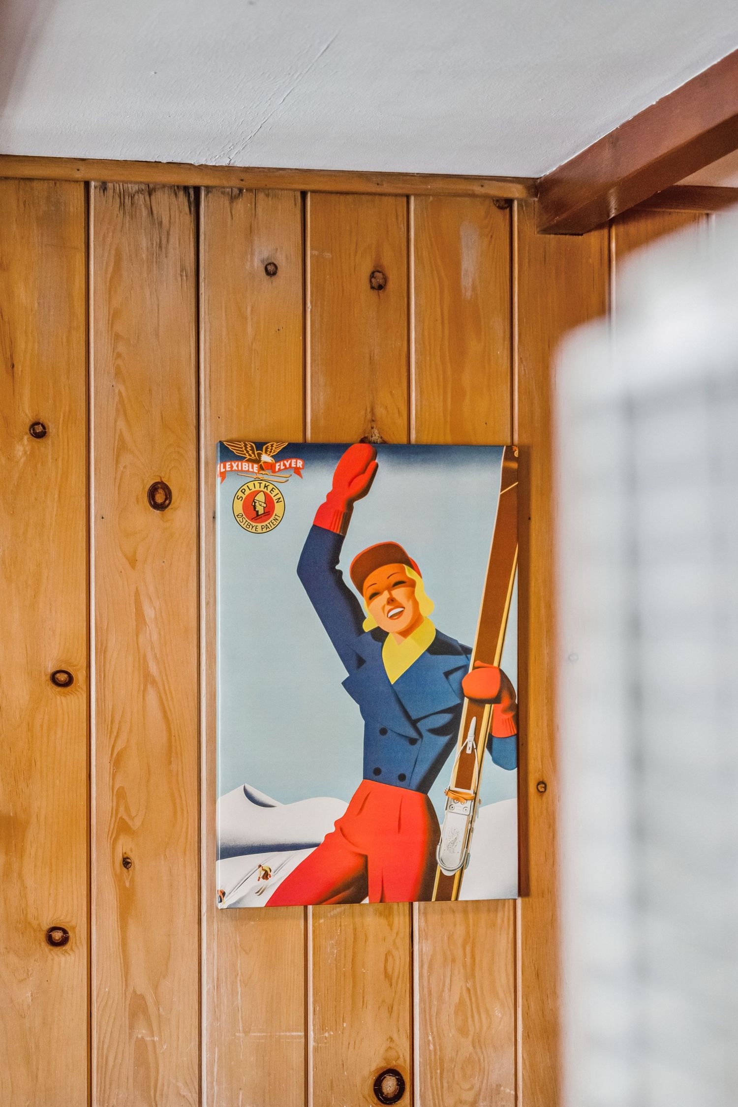 Vintage retro ski poster of a skier on knotty pine wood-paneled cabin wall.