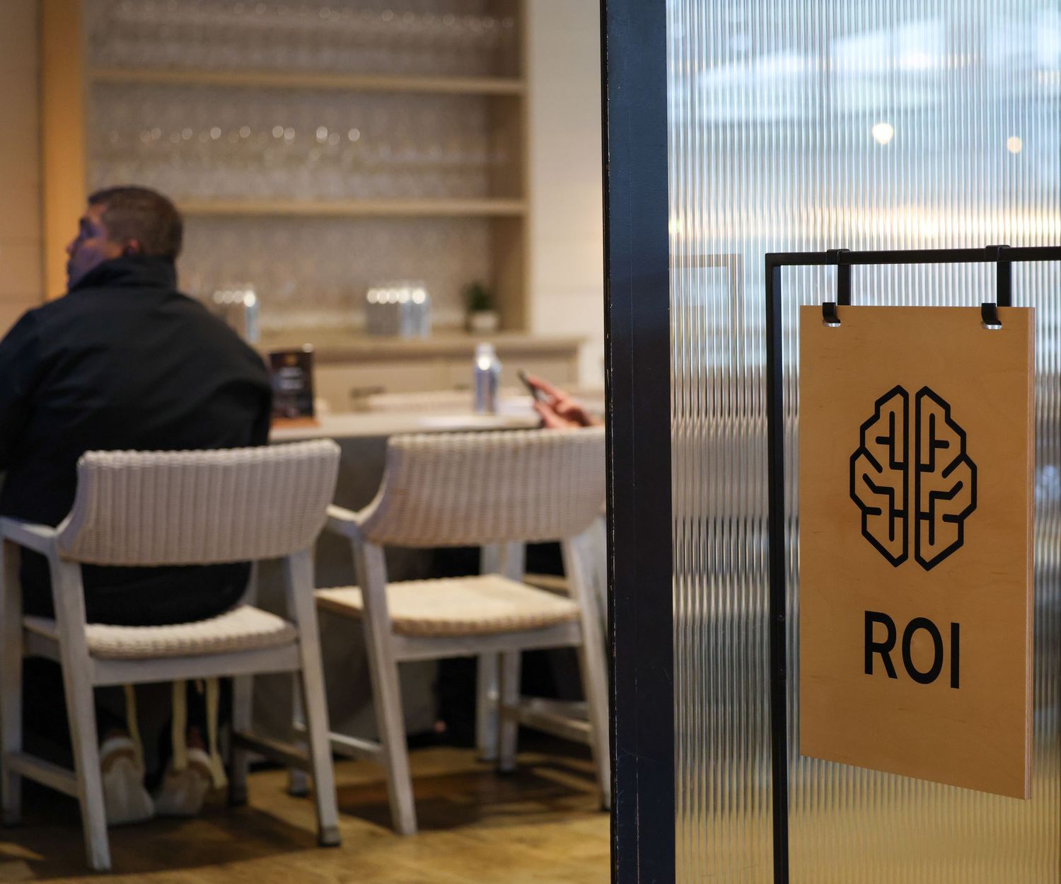 Man sitting at a table inside a modern office lounge with an ROI brain logo sign on a glass door.