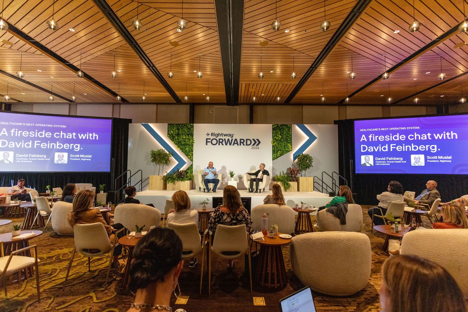 Attendees seated at a fireside chat with David Feinberg at a Forward conference in a modern wood-paneled venue.