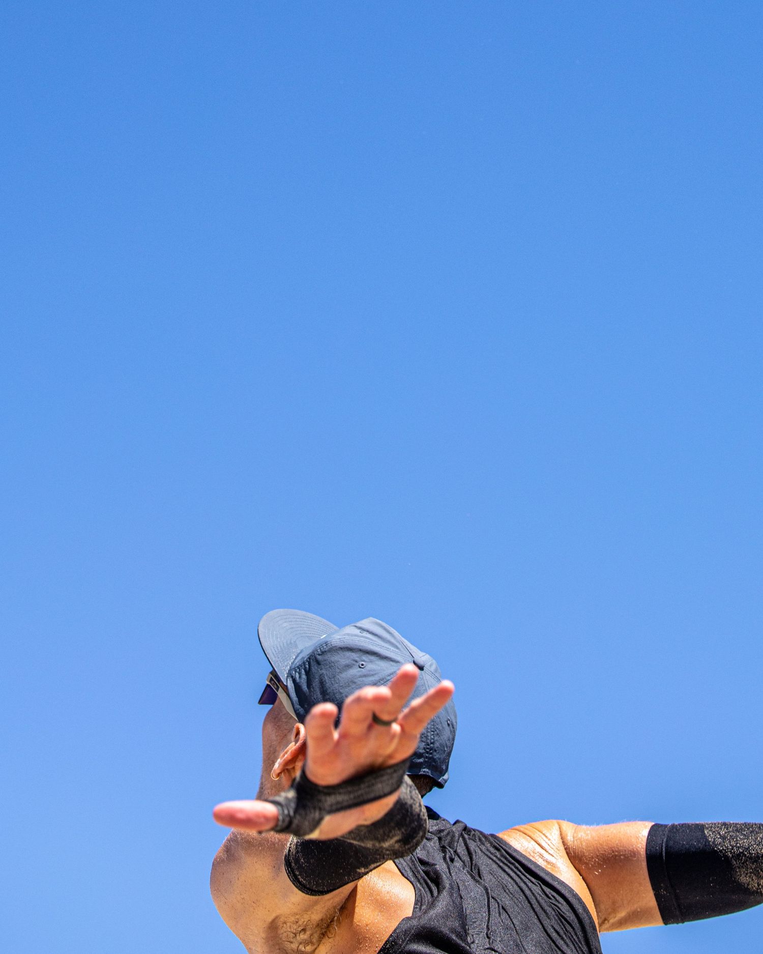 Person in dark athletic wear and cap reaches hand toward camera against clear blue sky.