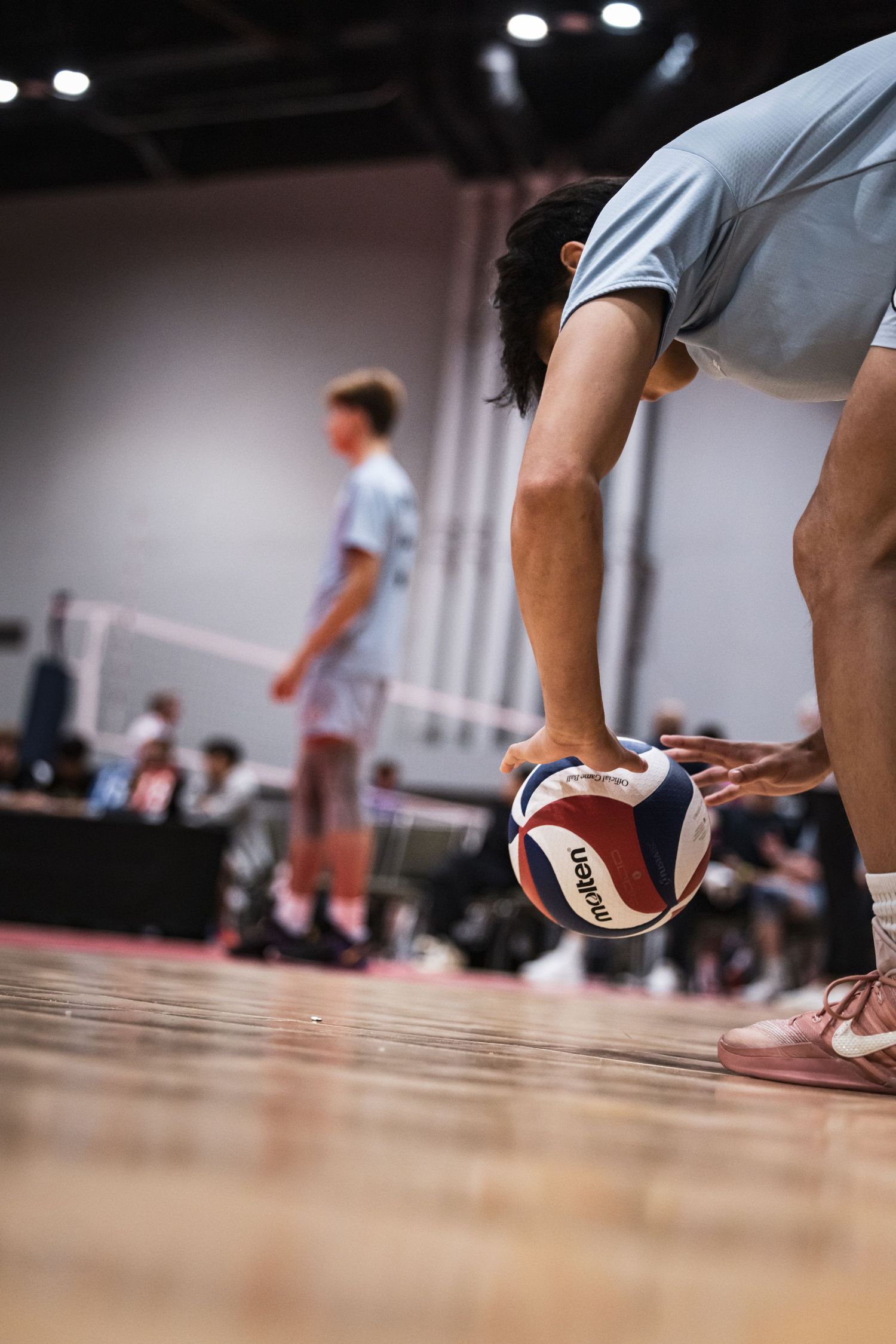 Player bending down to pick up a Molten volleyball on a hardwood court during an indoor volleyball match.