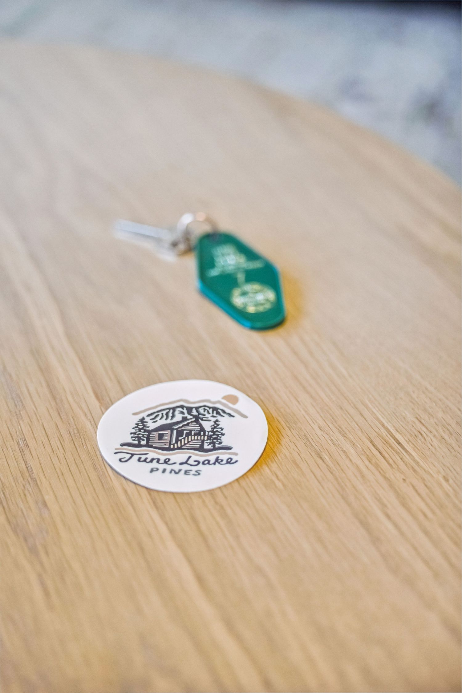 June Lake Pines logo sticker and green vintage motel keychain on a light wood table surface.