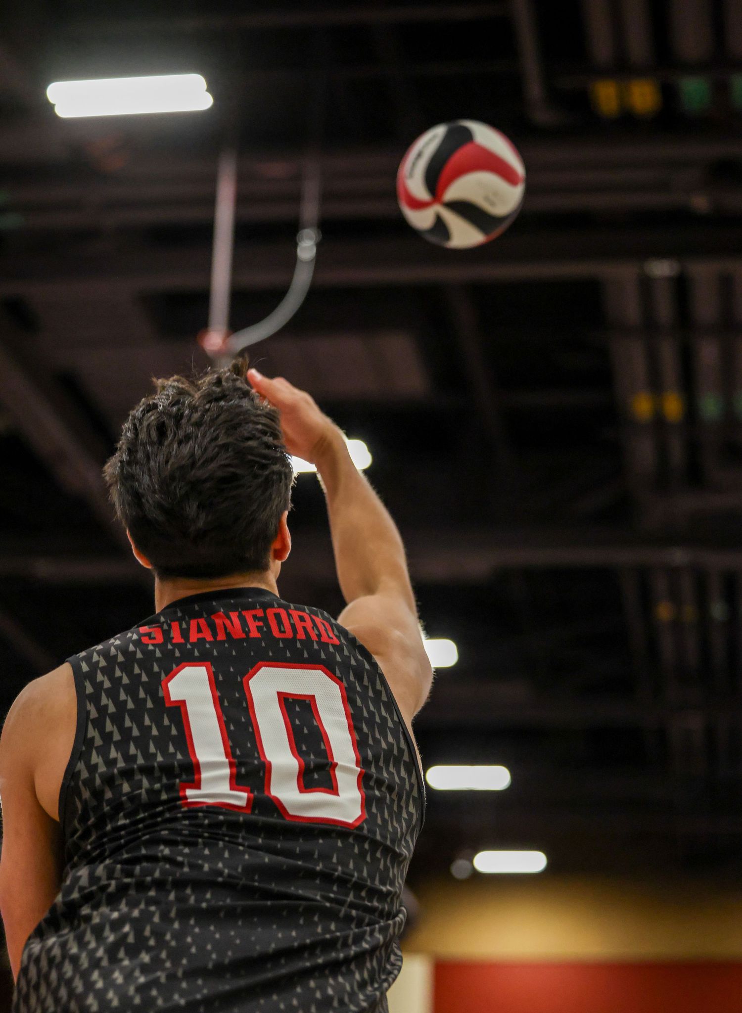 Stanford #10 volleyball player serving the ball during an indoor match.