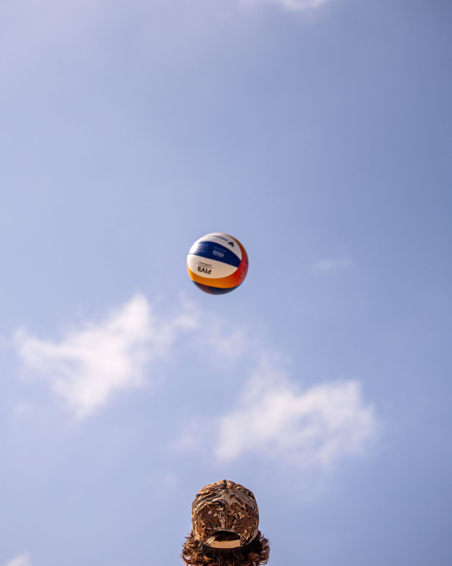 A colorful volleyball soaring high against a blue sky above an ornate golden statue outdoors.