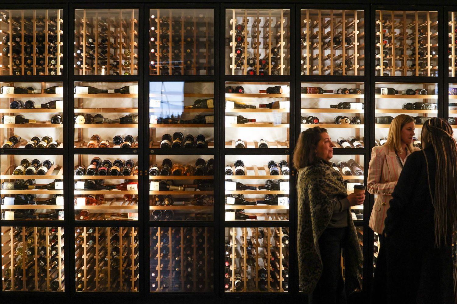Guests browsing an illuminated floor-to-ceiling wine cellar wall at a restaurant.