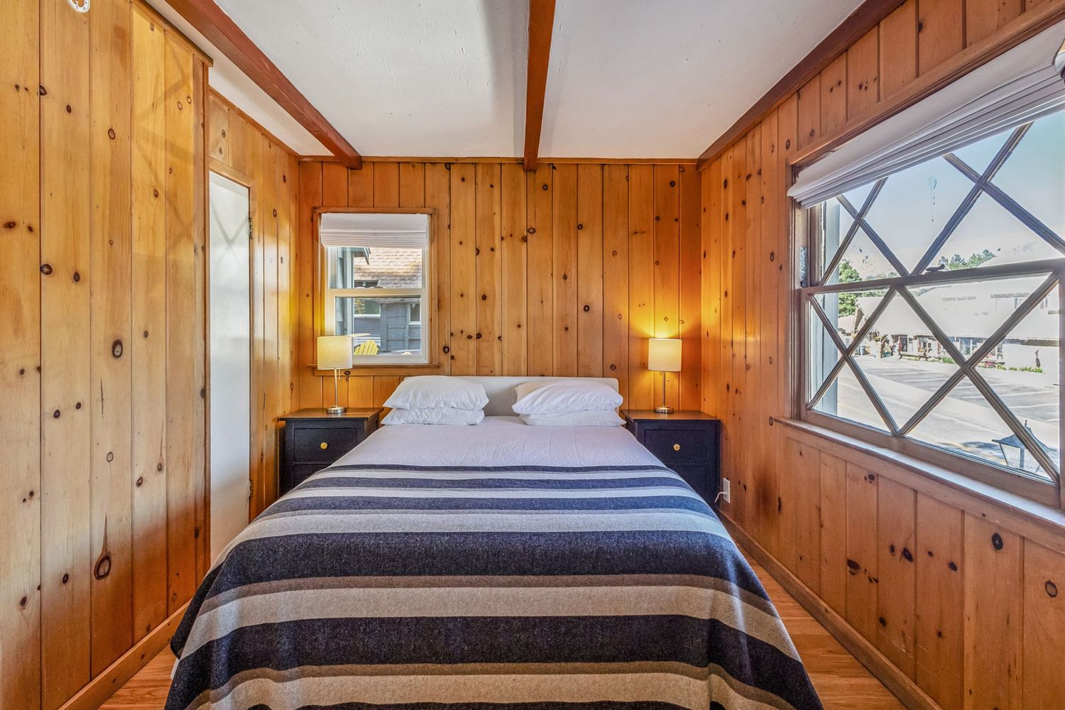 Cozy wood-paneled bedroom with a queen bed, striped blanket, and two nightstand lamps in a rustic cabin.