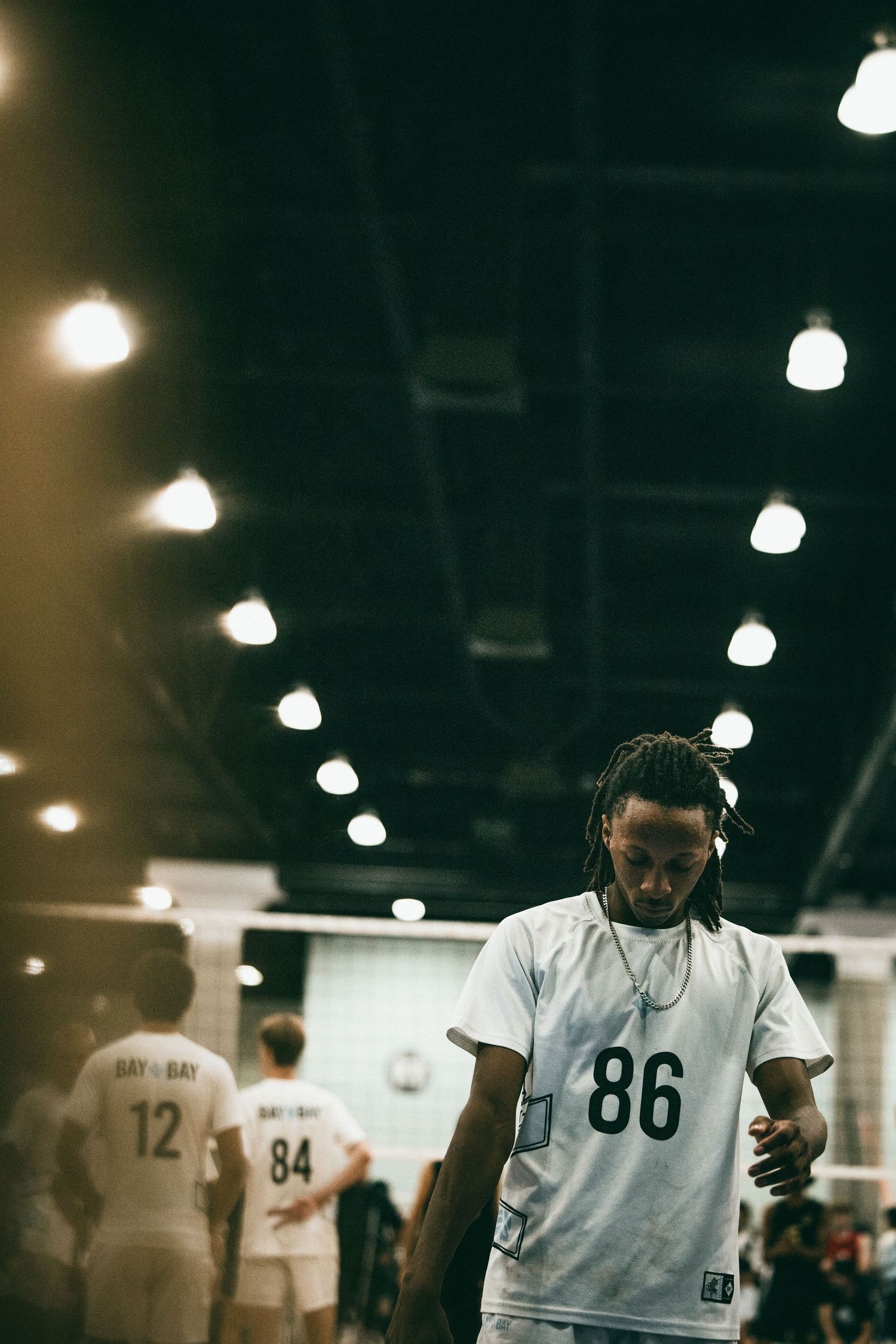 Player wearing jersey number 86 stands in an indoor sports arena with teammates in white uniforms visible in background.