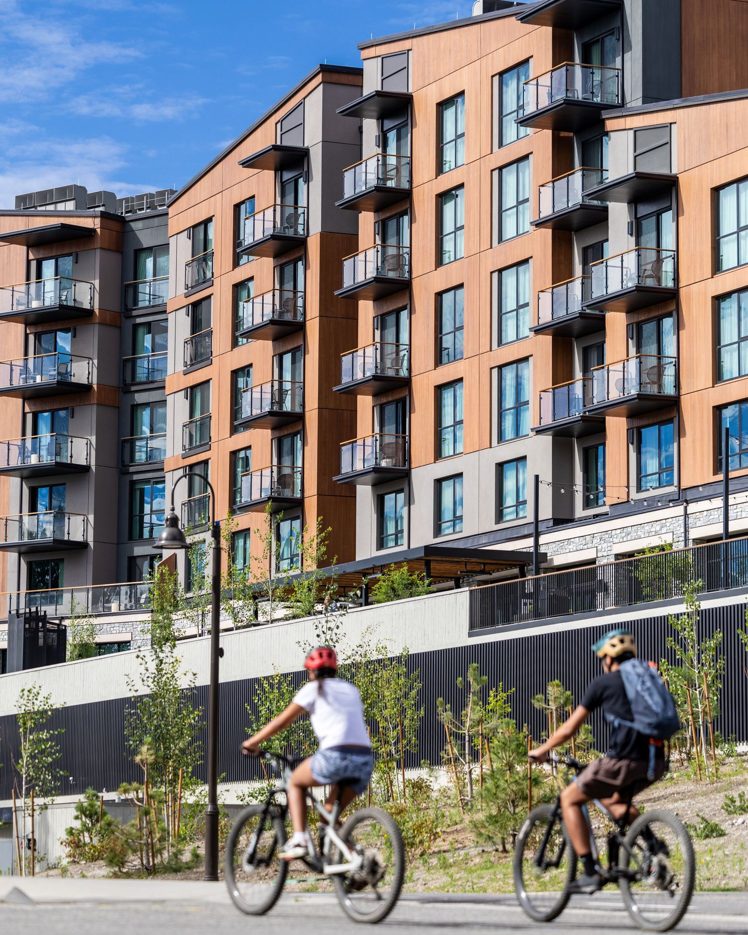 Two cyclists riding past modern brick apartment complex.