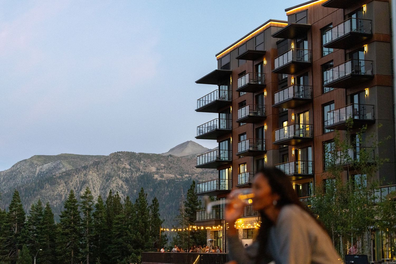 Contemporary mountain resort hotel at twilight with illuminated balconies and scenic peak backdrop.