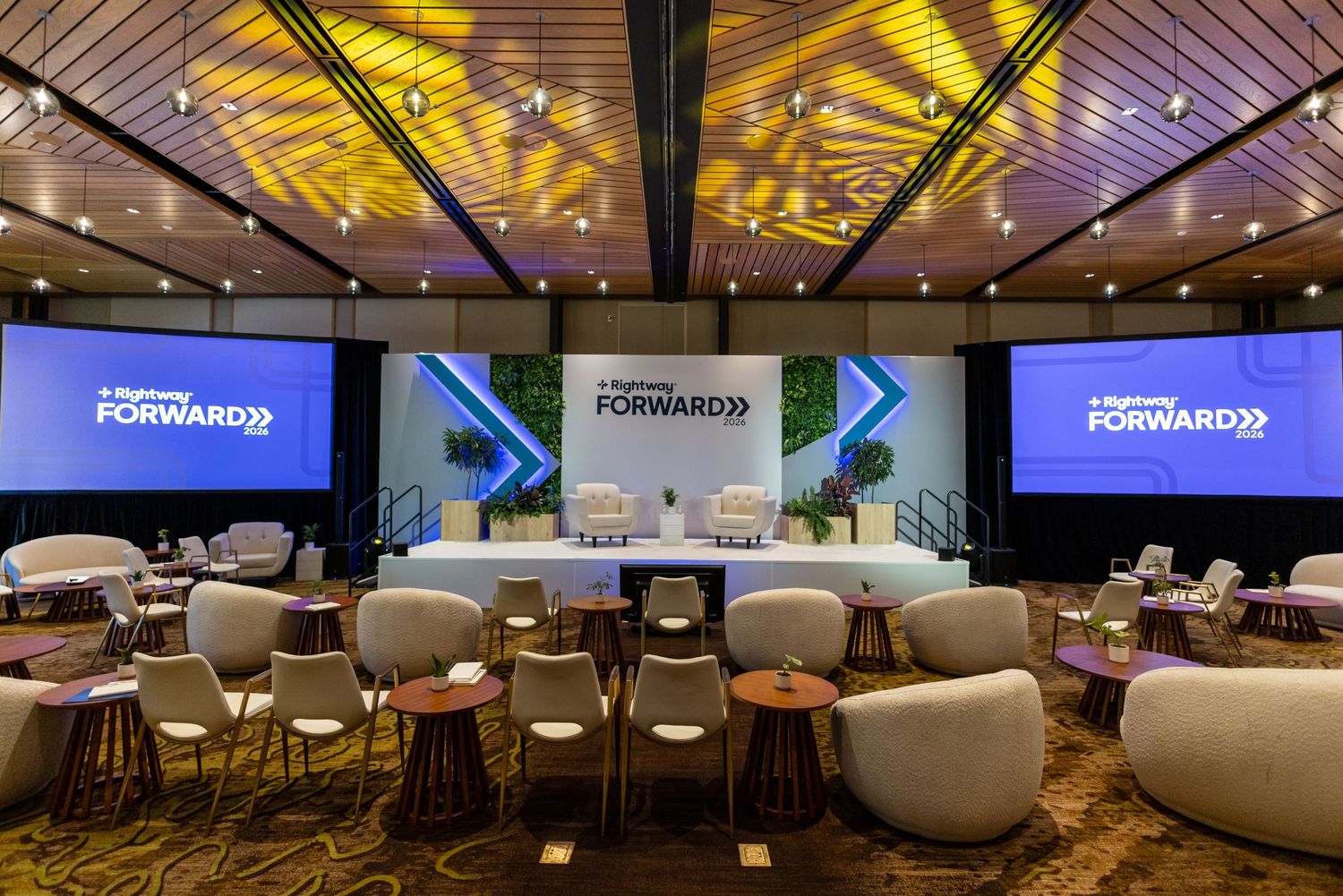 Modern conference hall with blue screens displaying Forward 22 event signage, stylish lounge seating, and golden ceiling lights.