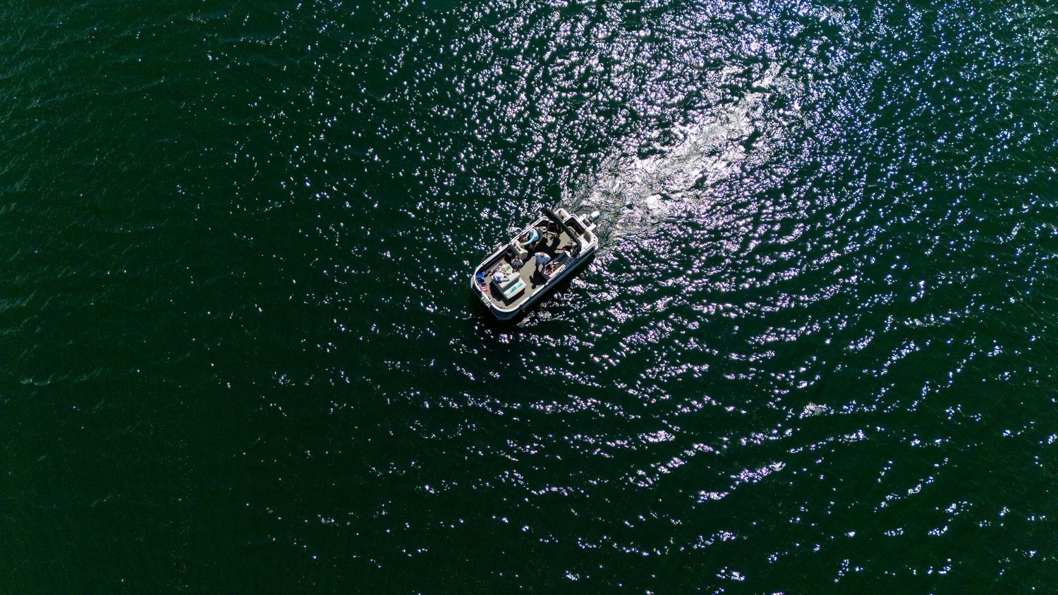 Aerial view of a motorboat creating ripples on deep green lake water from above.