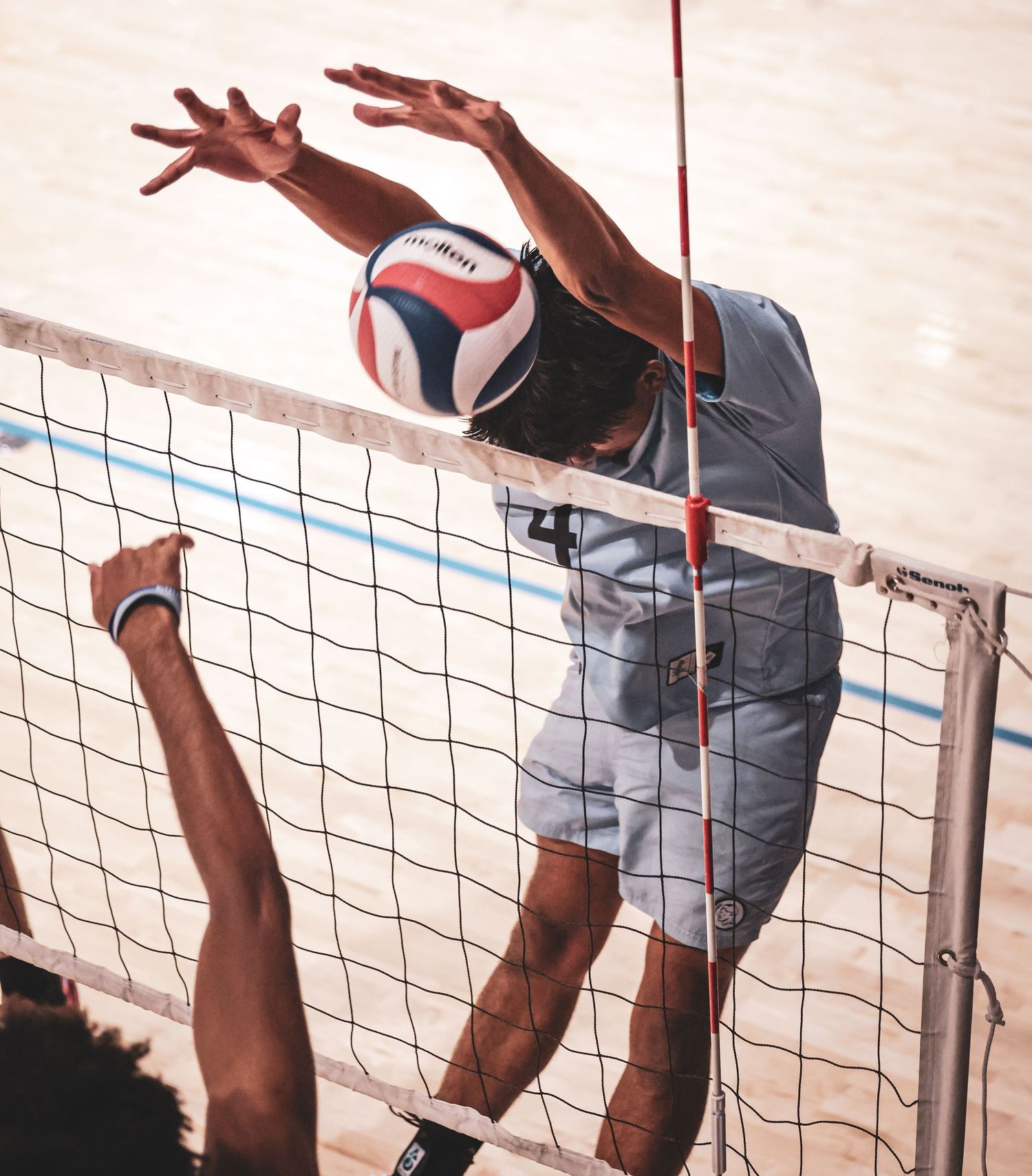 A volleyball player leaps to spike the ball over the net during an intense indoor volleyball match.