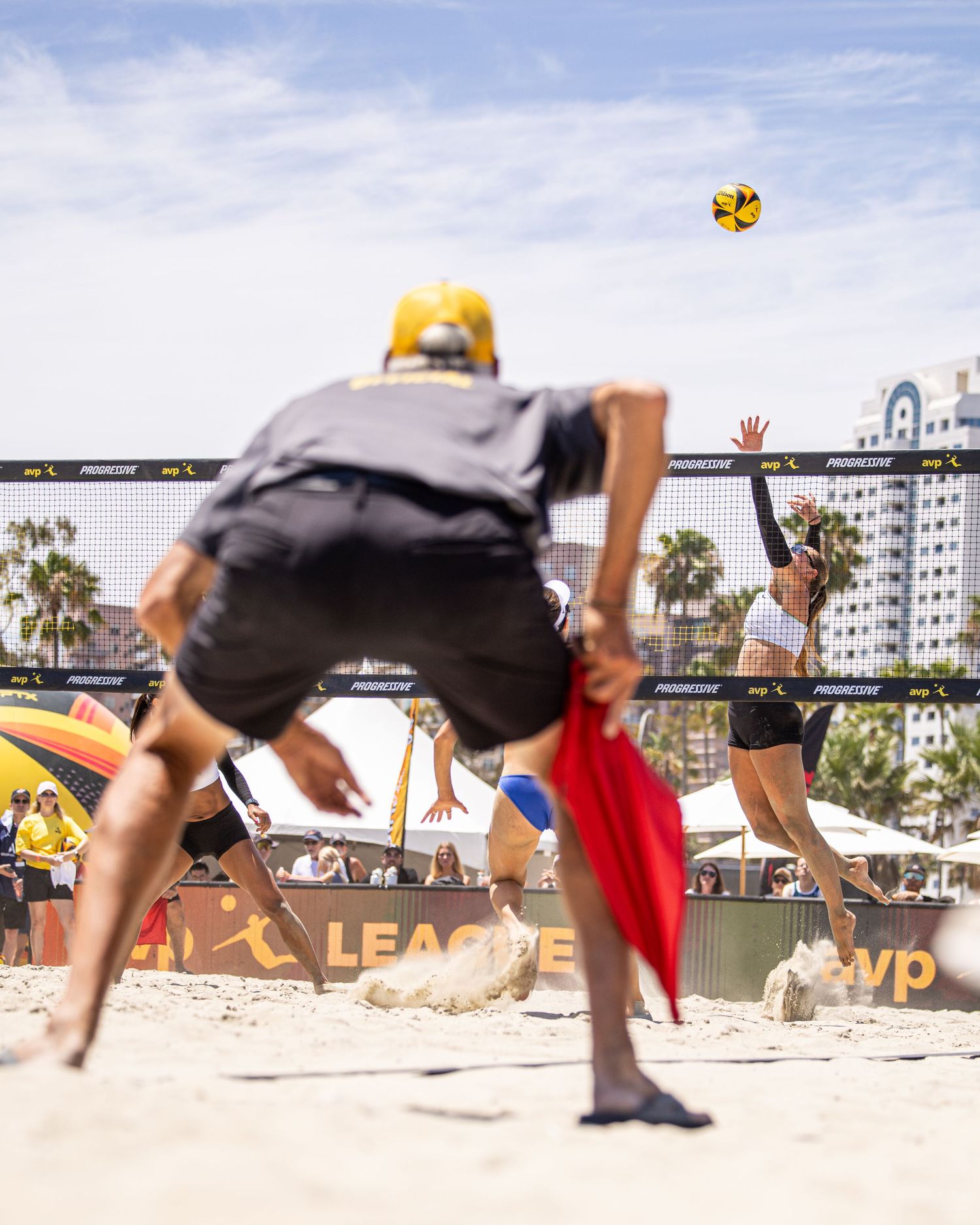 Beach volleyball players compete at a sandy outdoor court during an AVP League tournament on a sunny day.