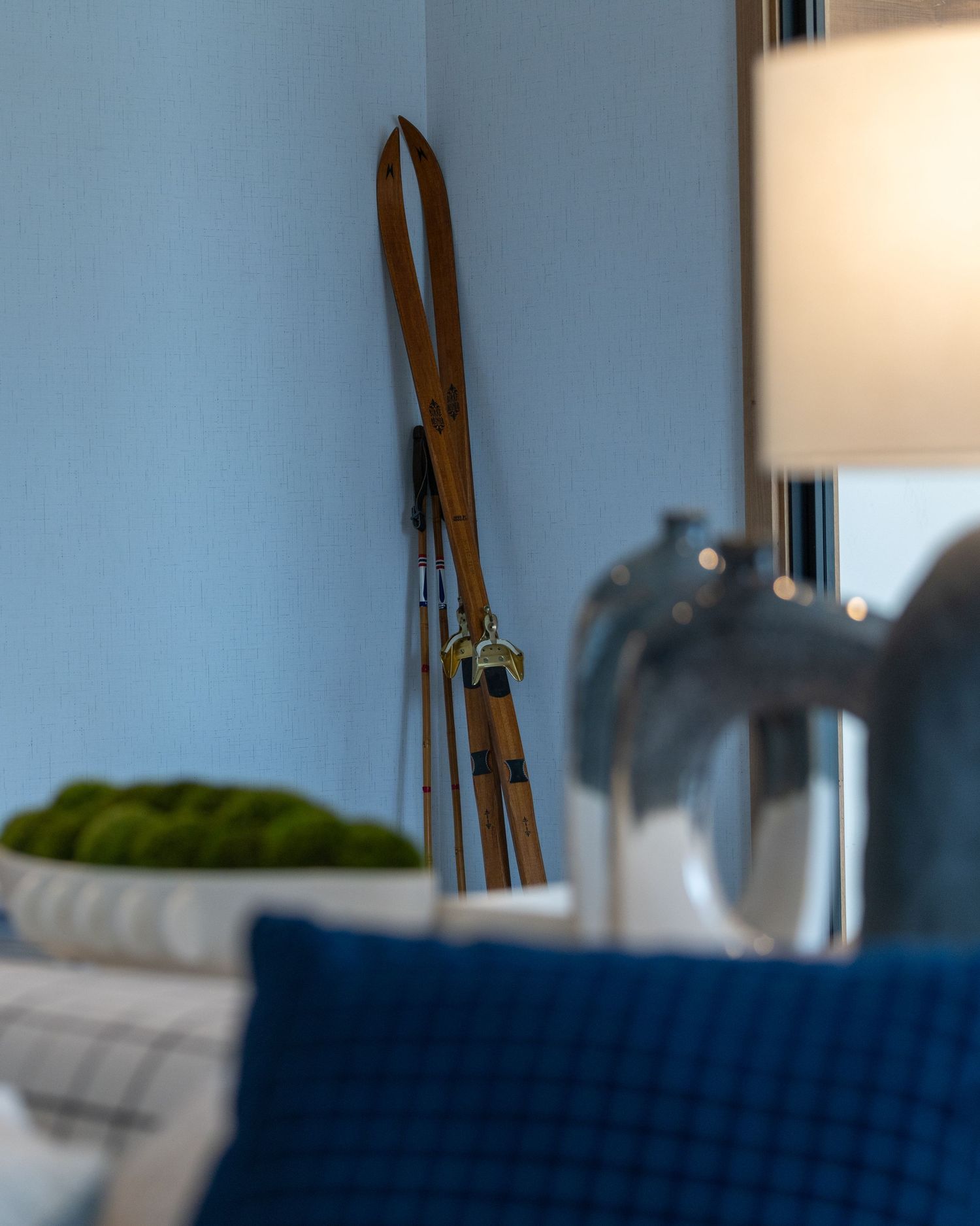 Vintage wooden skis leaning against a blue wall beside a lamp in a cozy interior.