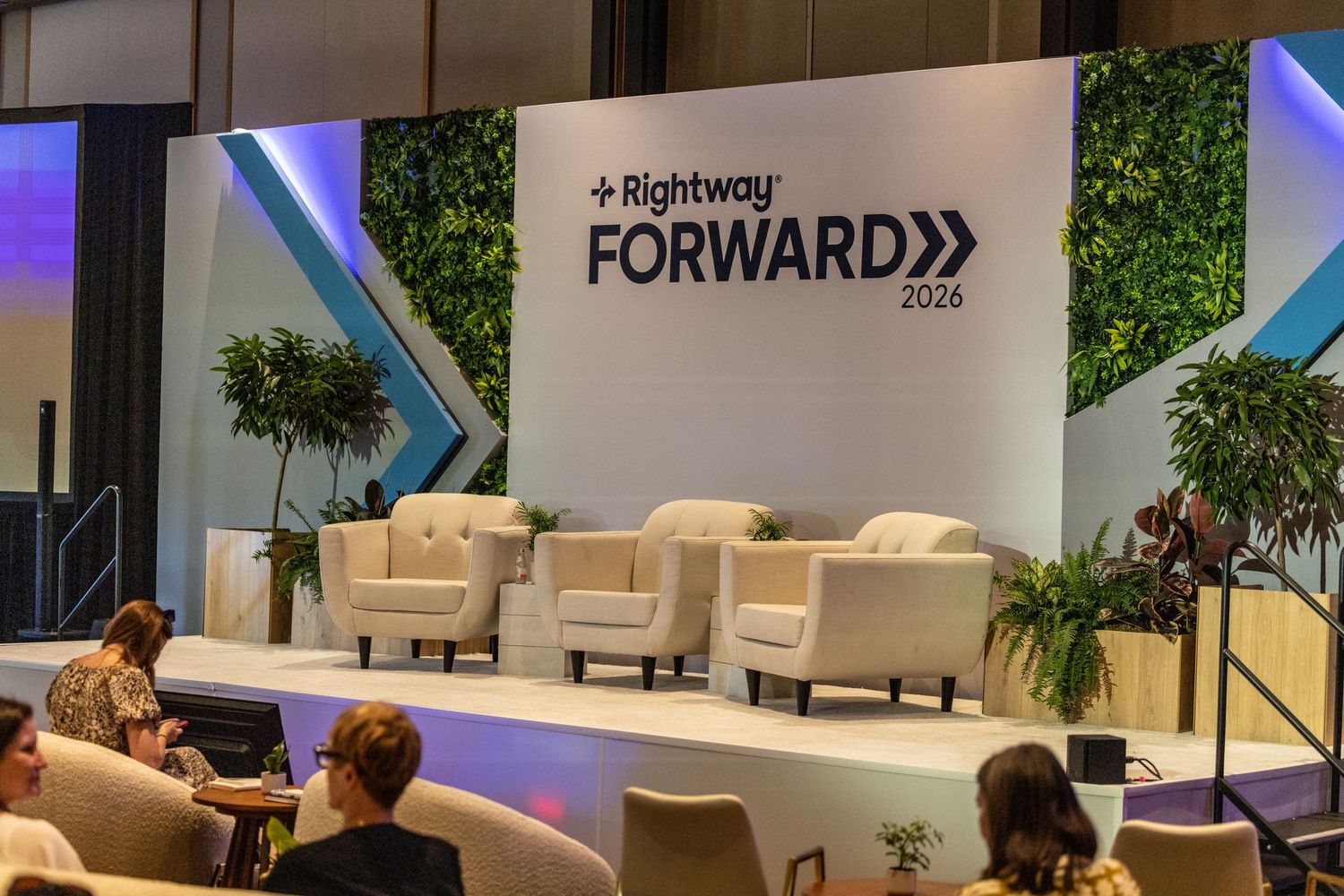 Stage setup for Rightway Forward 2026 event with white armchairs, green plants, and branded backdrop signage.