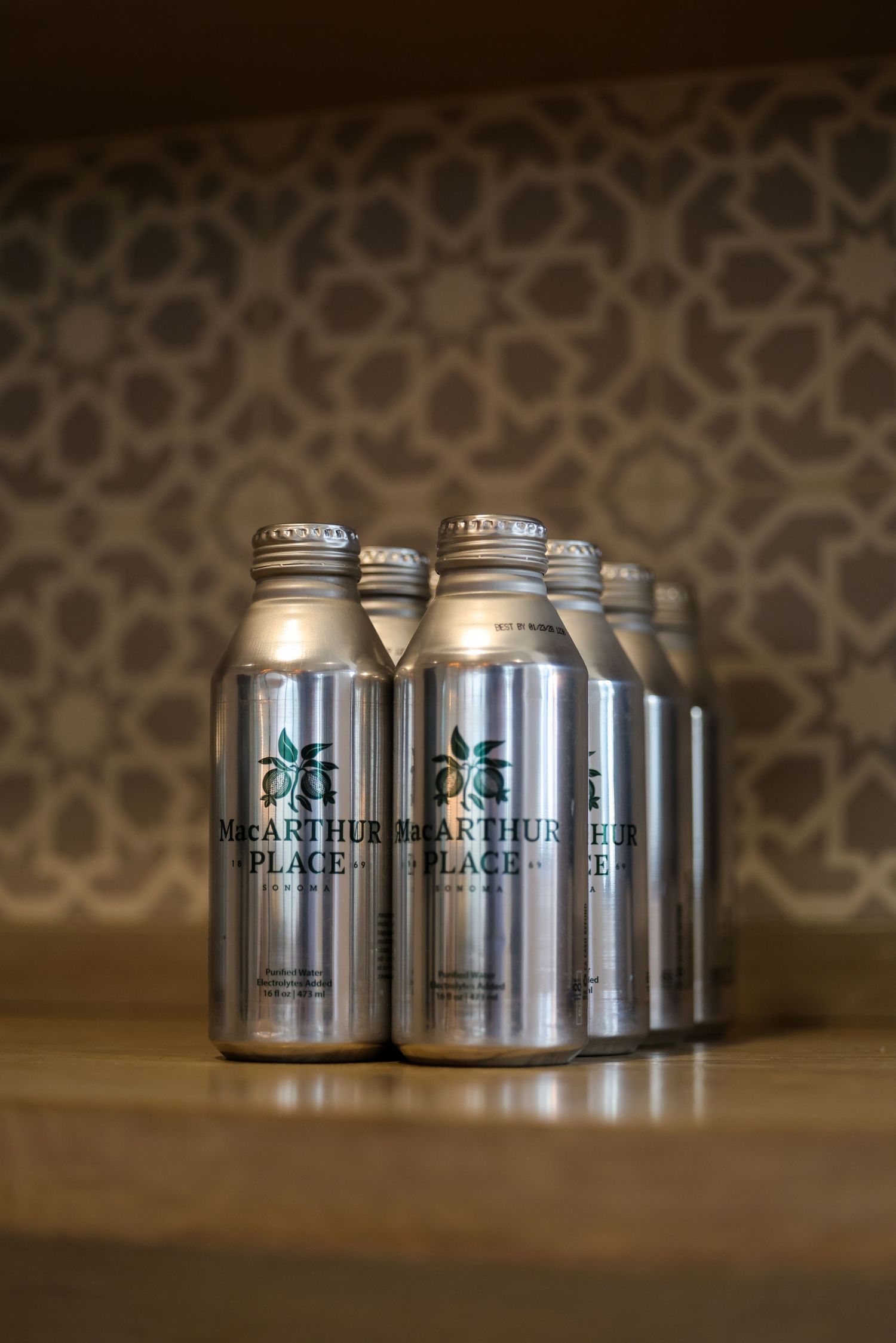 Six silver aluminum MacArthur Place branded water bottles grouped on a wooden surface.