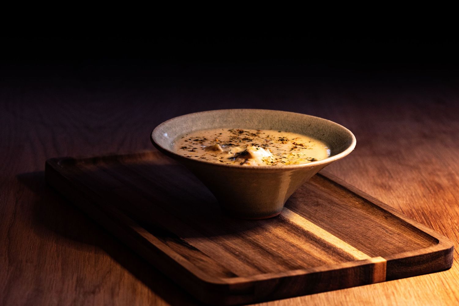 Rustic ceramic bowl of creamy soup on a wooden serving board in dramatic moody lighting.