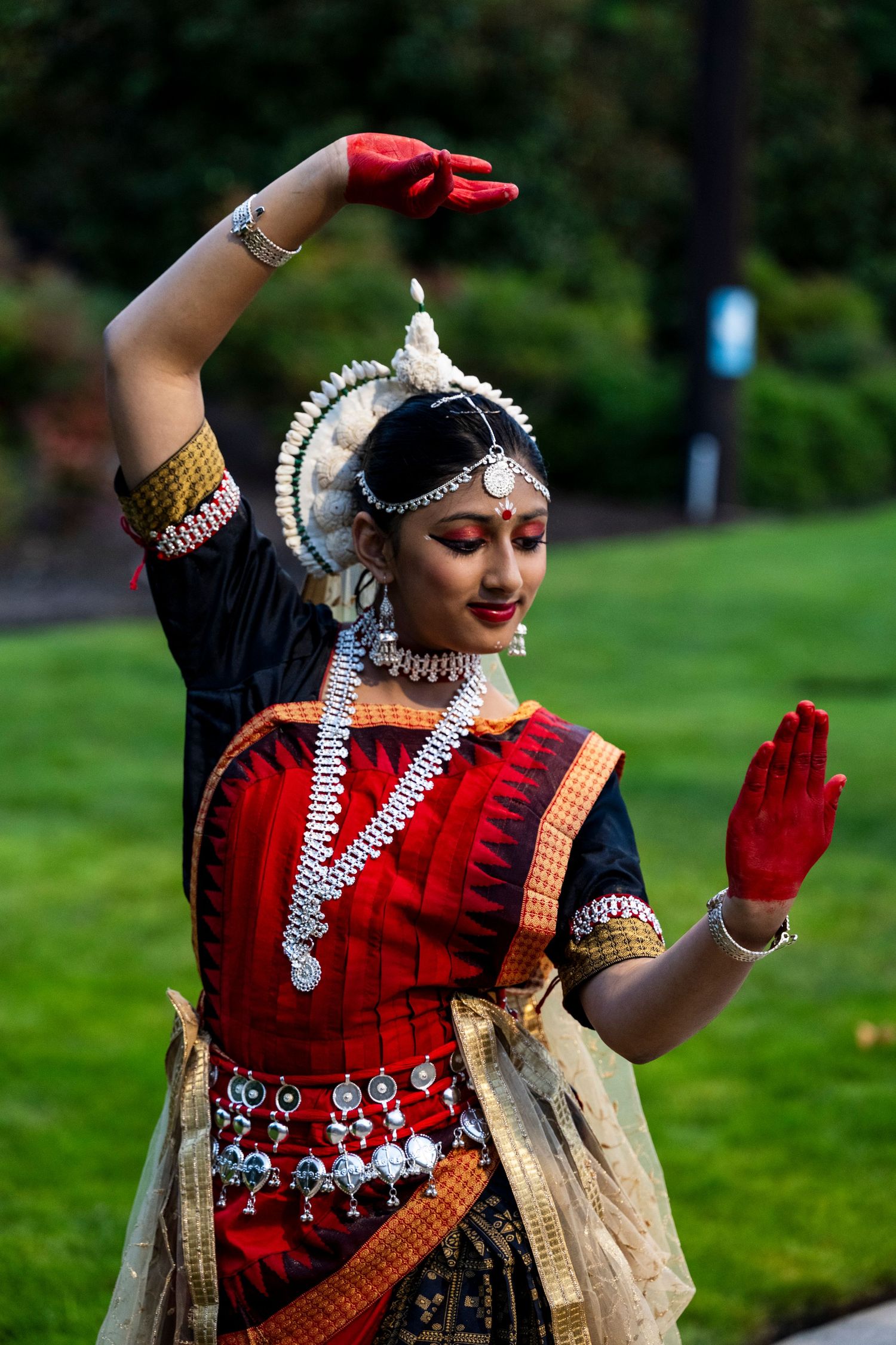 Woman performing classical Odissi dance in traditional red costume and silver jewelry outdoors.