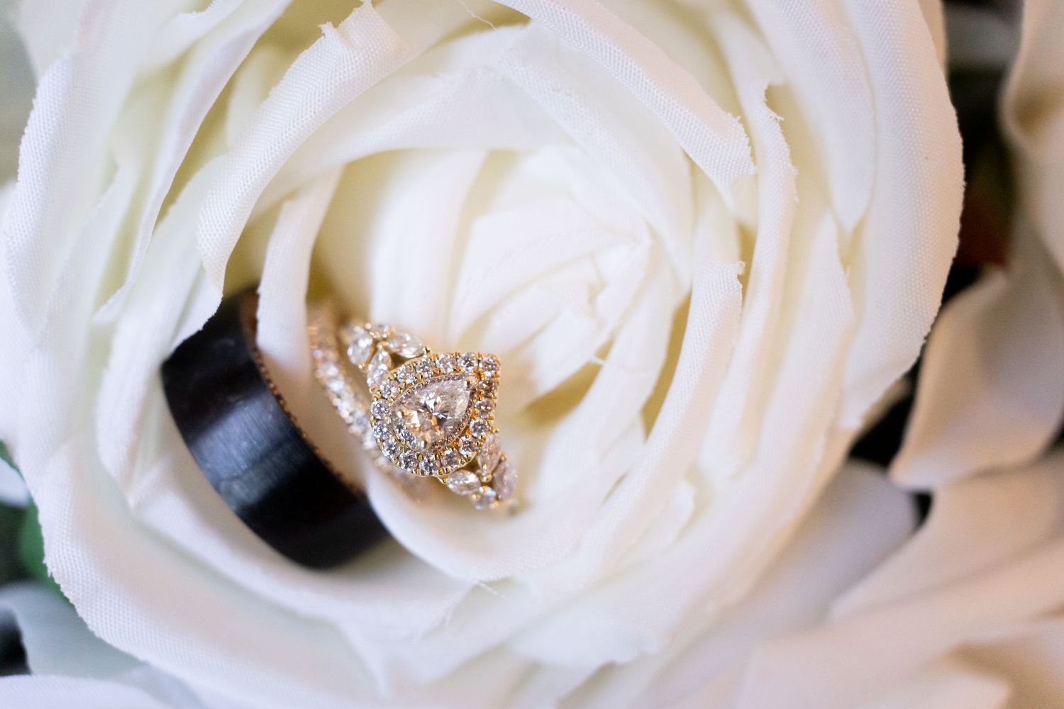 Elegant diamond halo engagement ring nestled in the petals of a white rose bouquet.