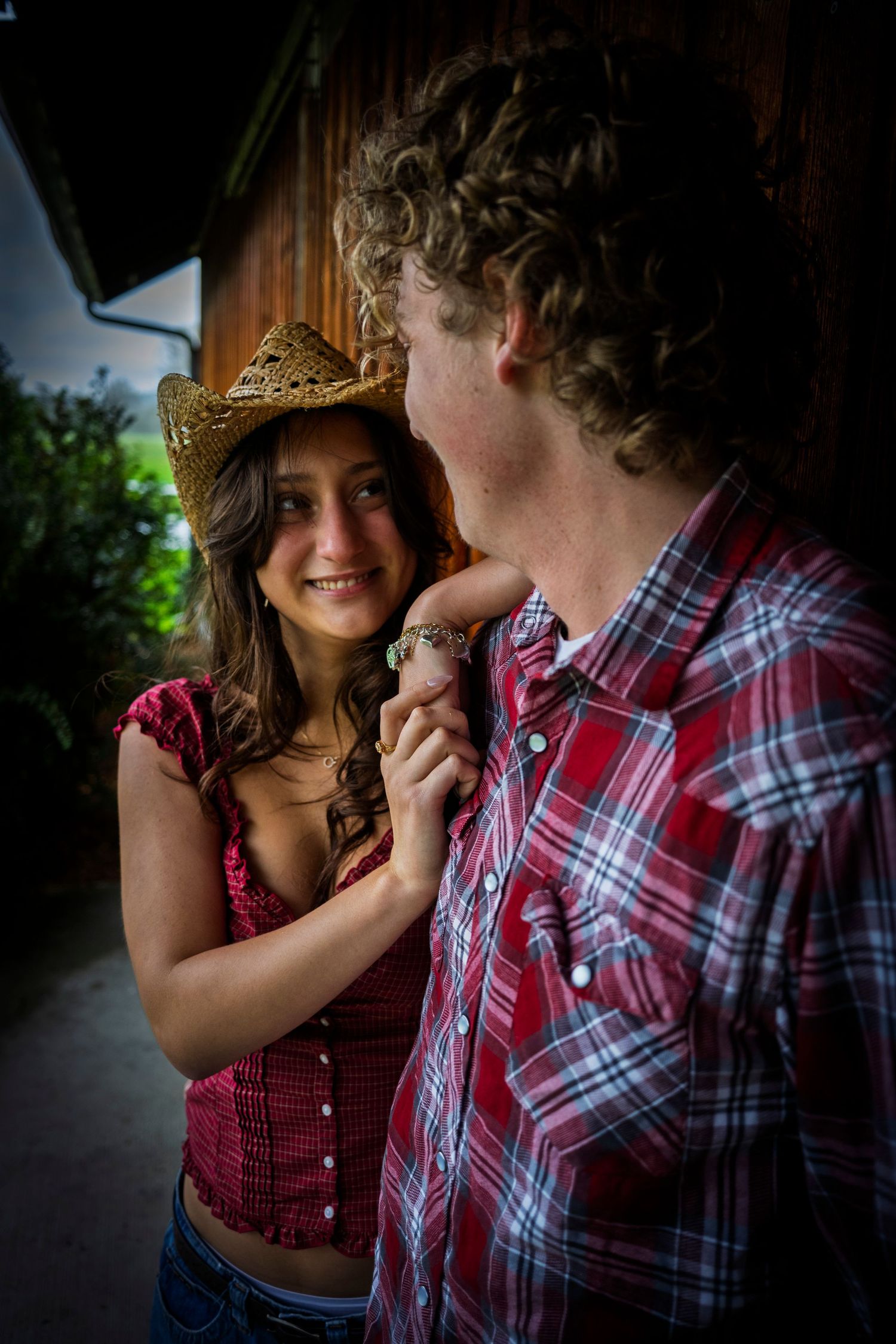 Young couple in country style clothing share a tender moment near a barn.
