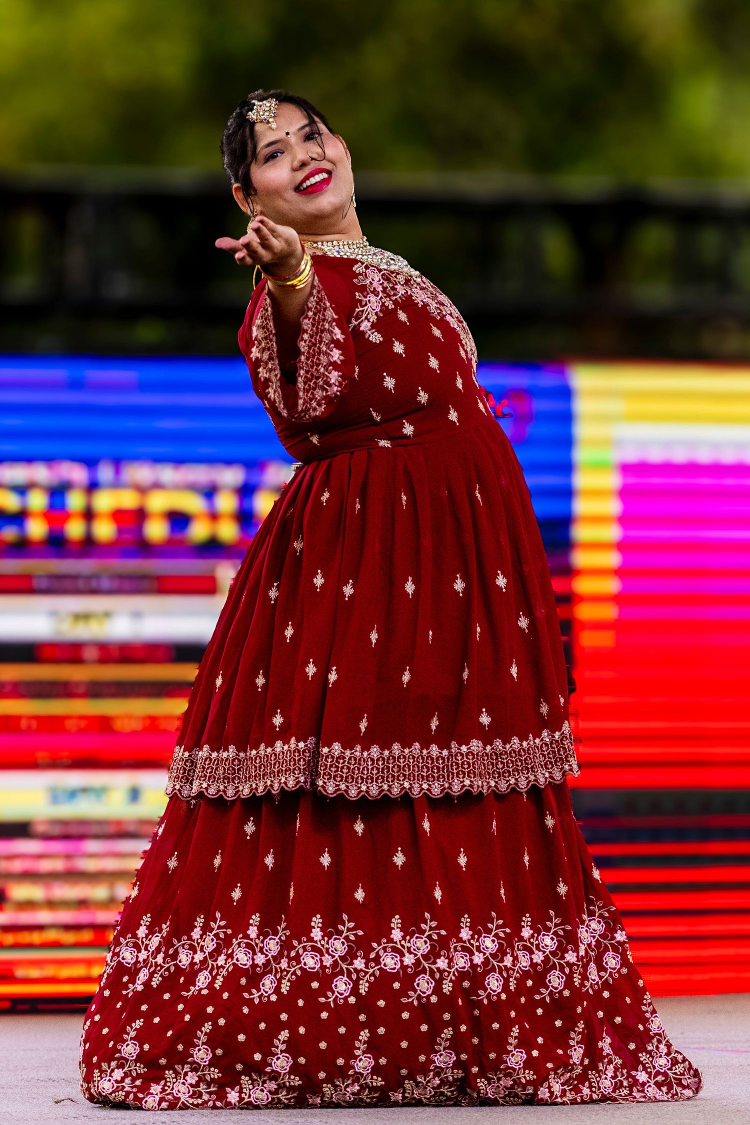 Woman performing Indian classical dance in an ornate red embroidered lehenga with traditional jewelry.