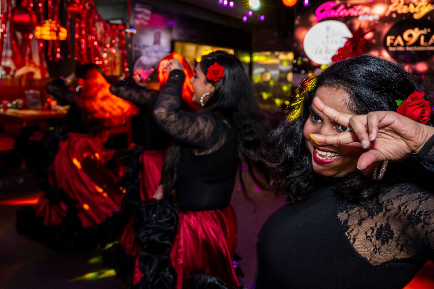 Vibrant flamenco party with dancers in red and black costumes under colorful lights.