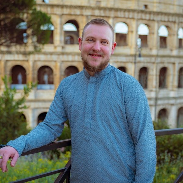 Happy man in blue patterned shirt smiling in front of the Roman Colosseum in Italy.