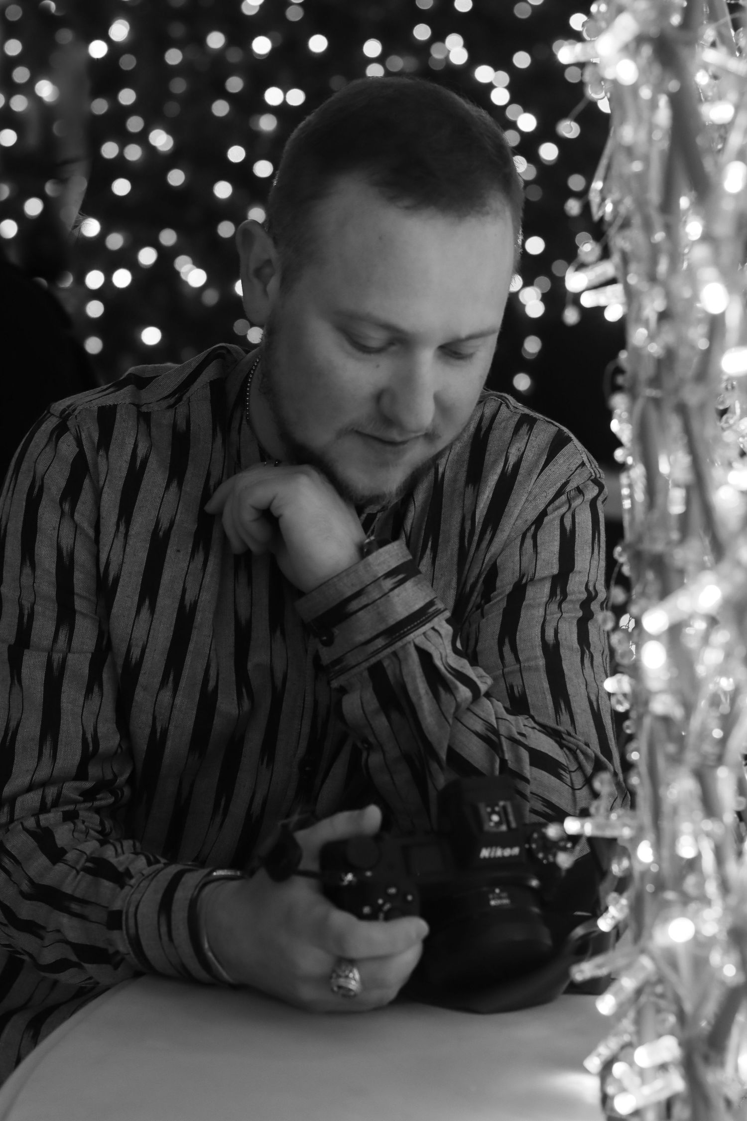 Black and white photo of man in striped shirt reviewing photos on Nikon camera.