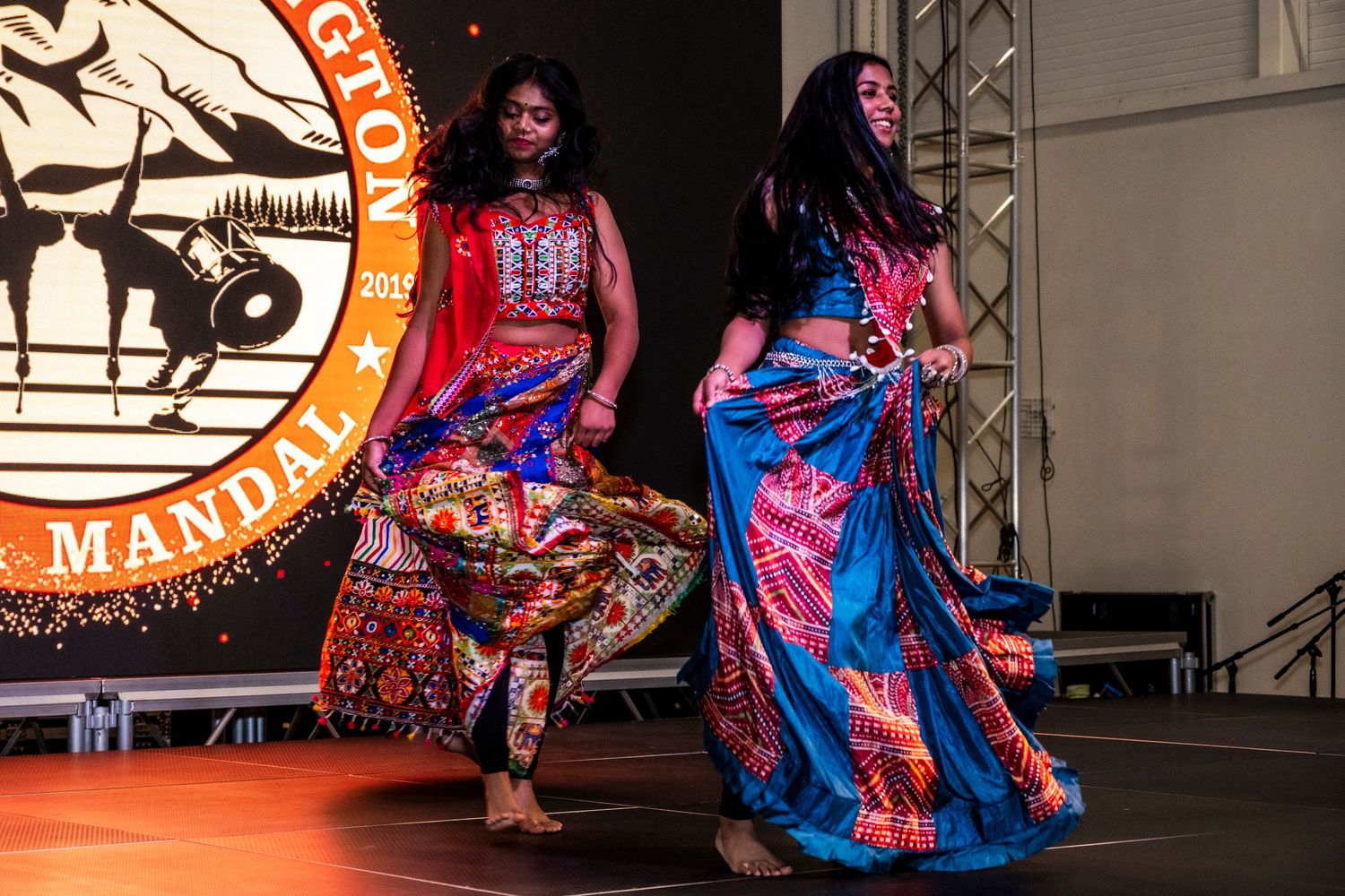Two women performing traditional Indian dance on stage in vibrant colorful costumes at a cultural festival.