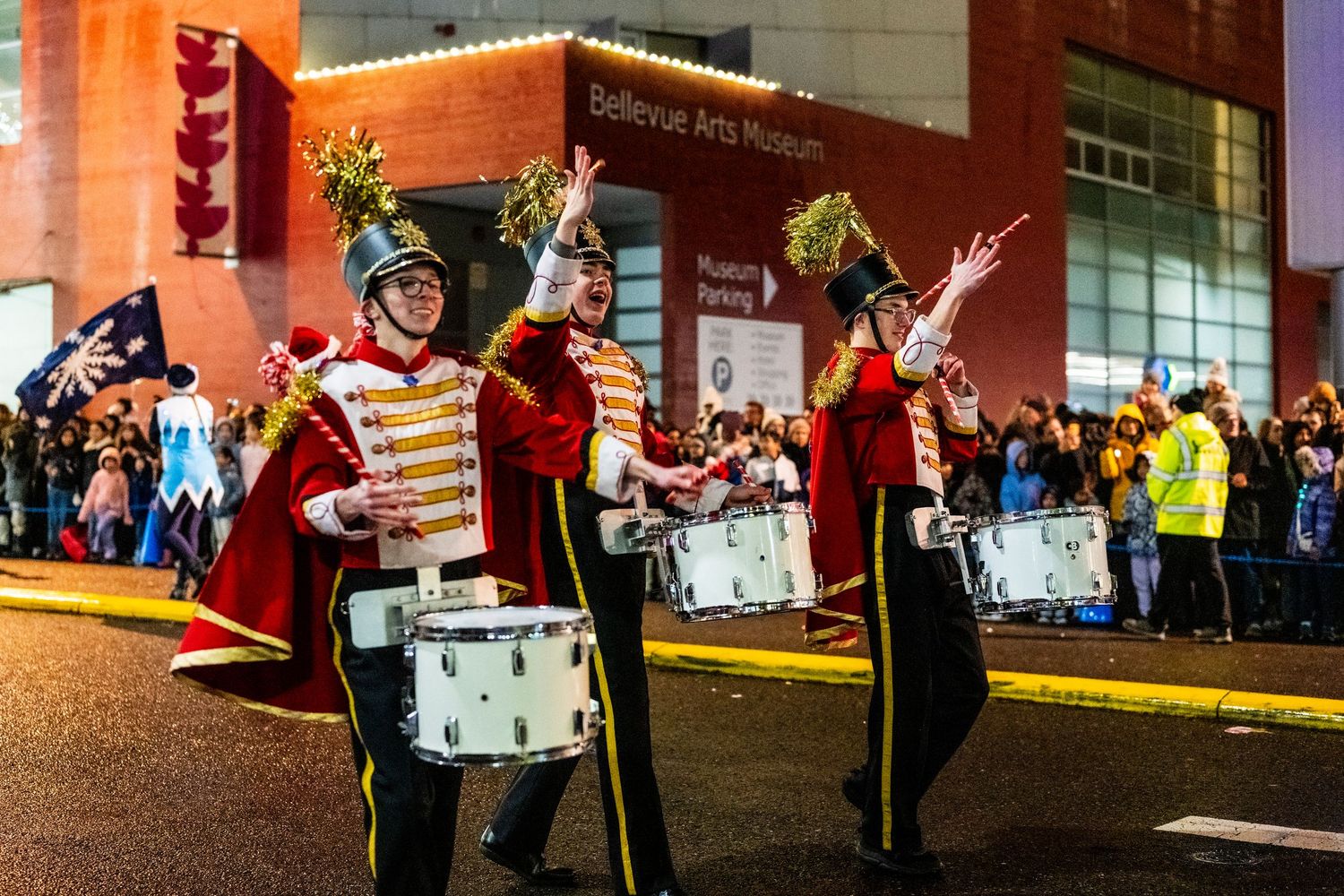 Marching band drummers in red uniforms performing at night parade near Bellevue Arts Museum.