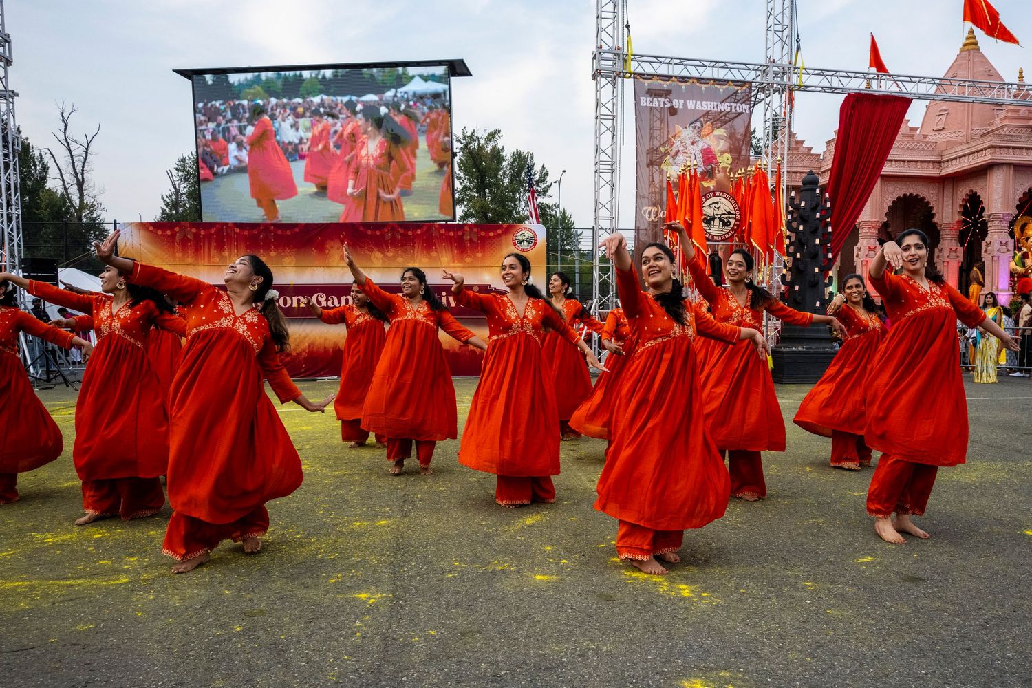 Group of female dancers in red traditional Indian costumes perform energetically at a cultural festival.