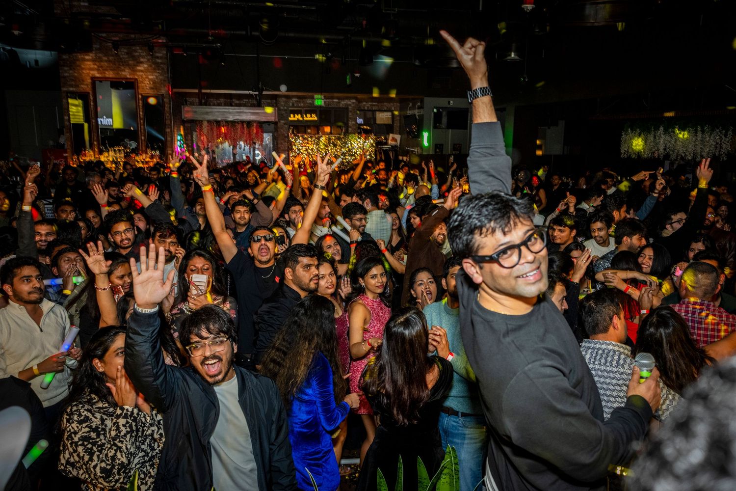A large crowd of young people celebrate with raised hands at an energetic indoor nightclub party event.