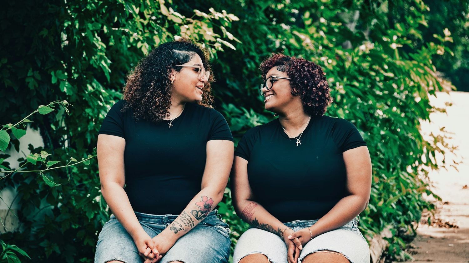 Two young women in black shirts sitting together outdoors smiling at each other for senior photos.